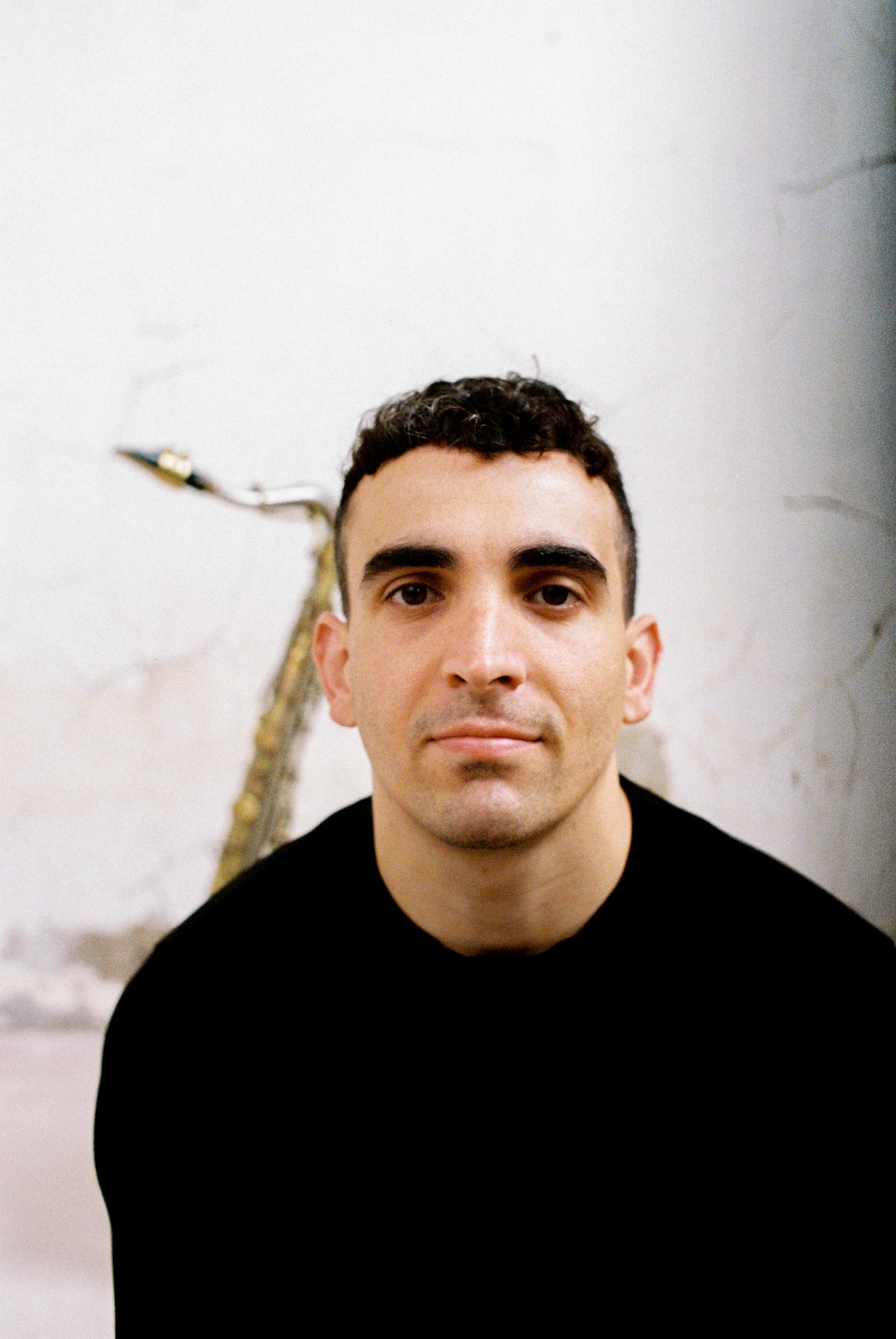 Man with short hair smiling at camera with saxophone in the background