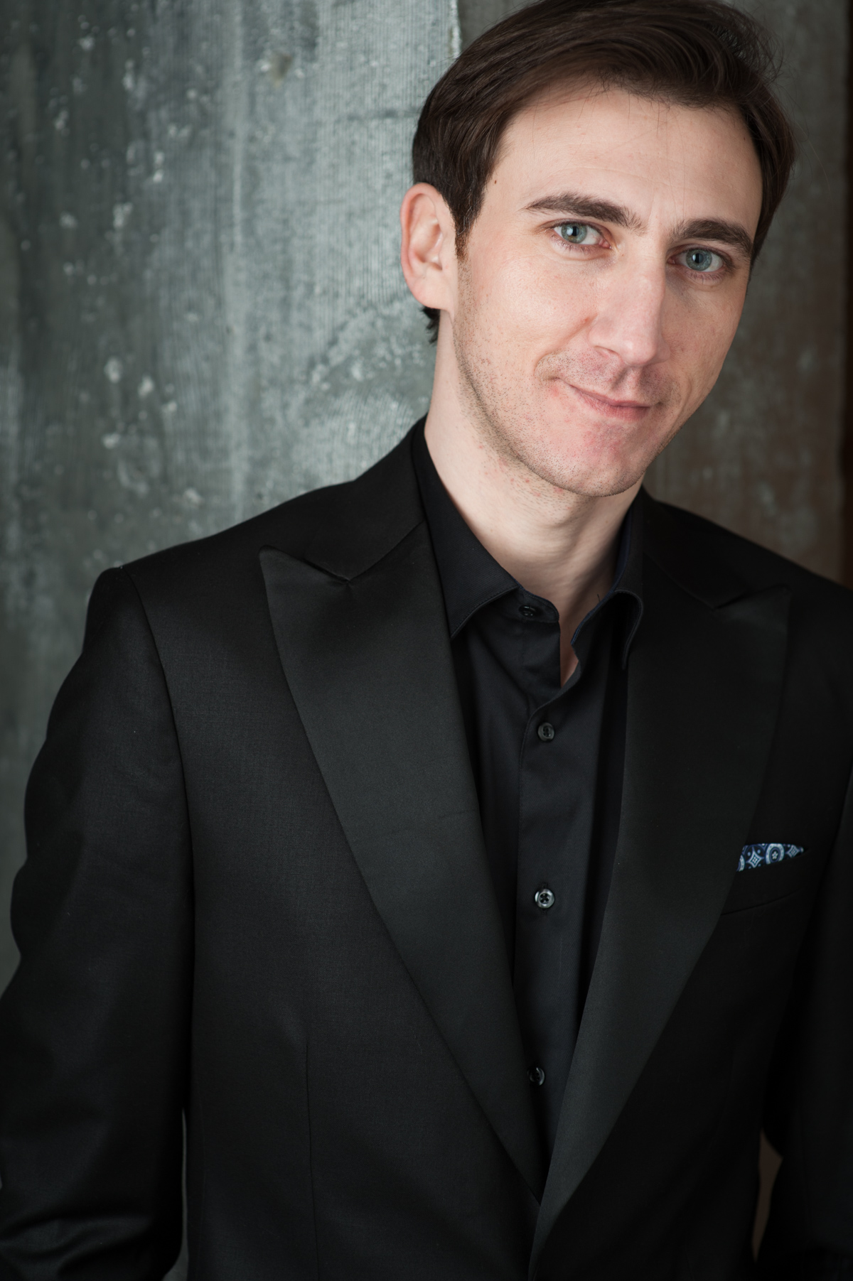 Man leaning against wall in dark suit smiling at camera