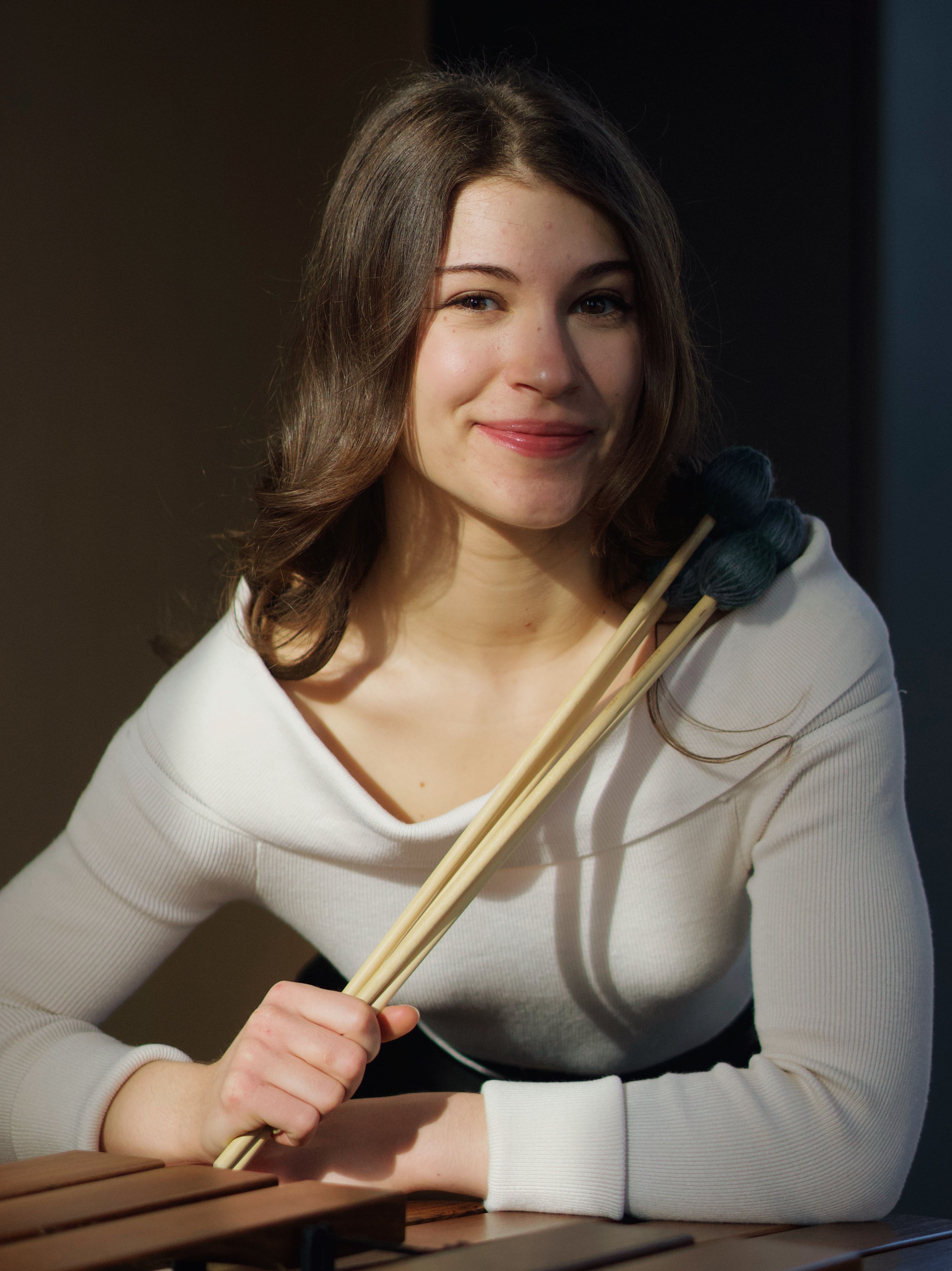Woman holding drum sticks in front of her while smiling at camera