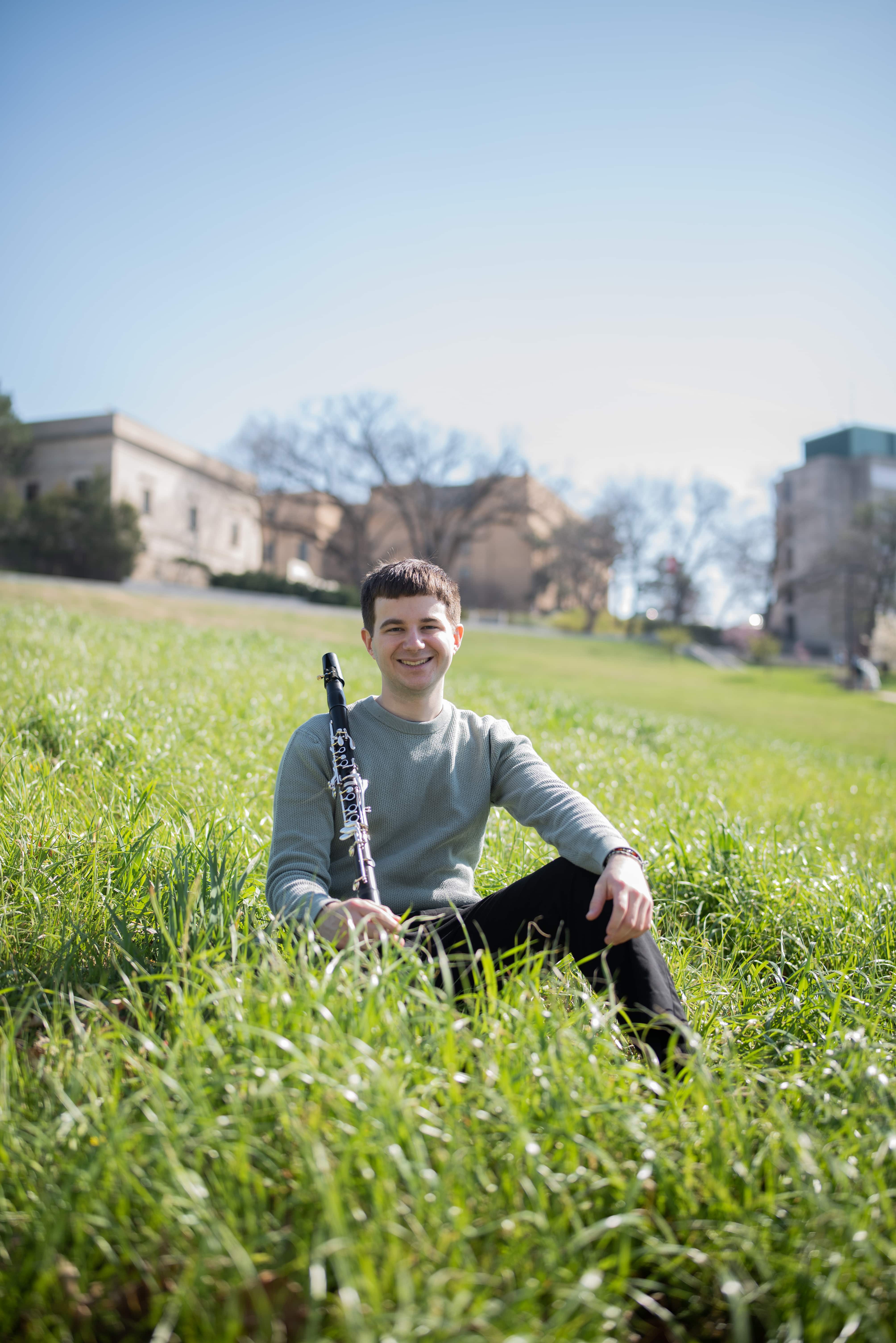 Clarinetist sitting in long grass in a field in front of houses