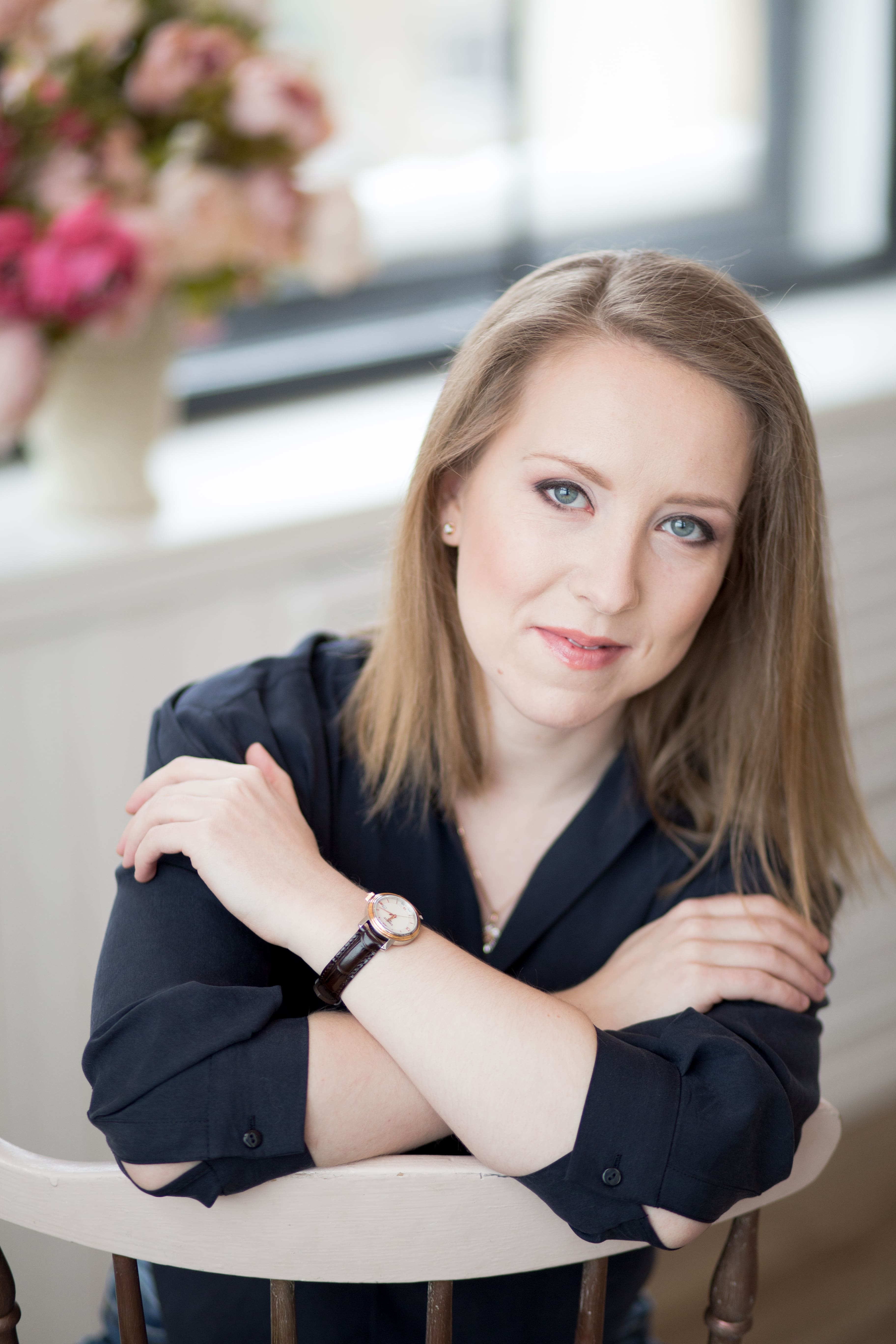 Woman sitting backwards on a chair smiling at the camera with arms crossed over shoulders