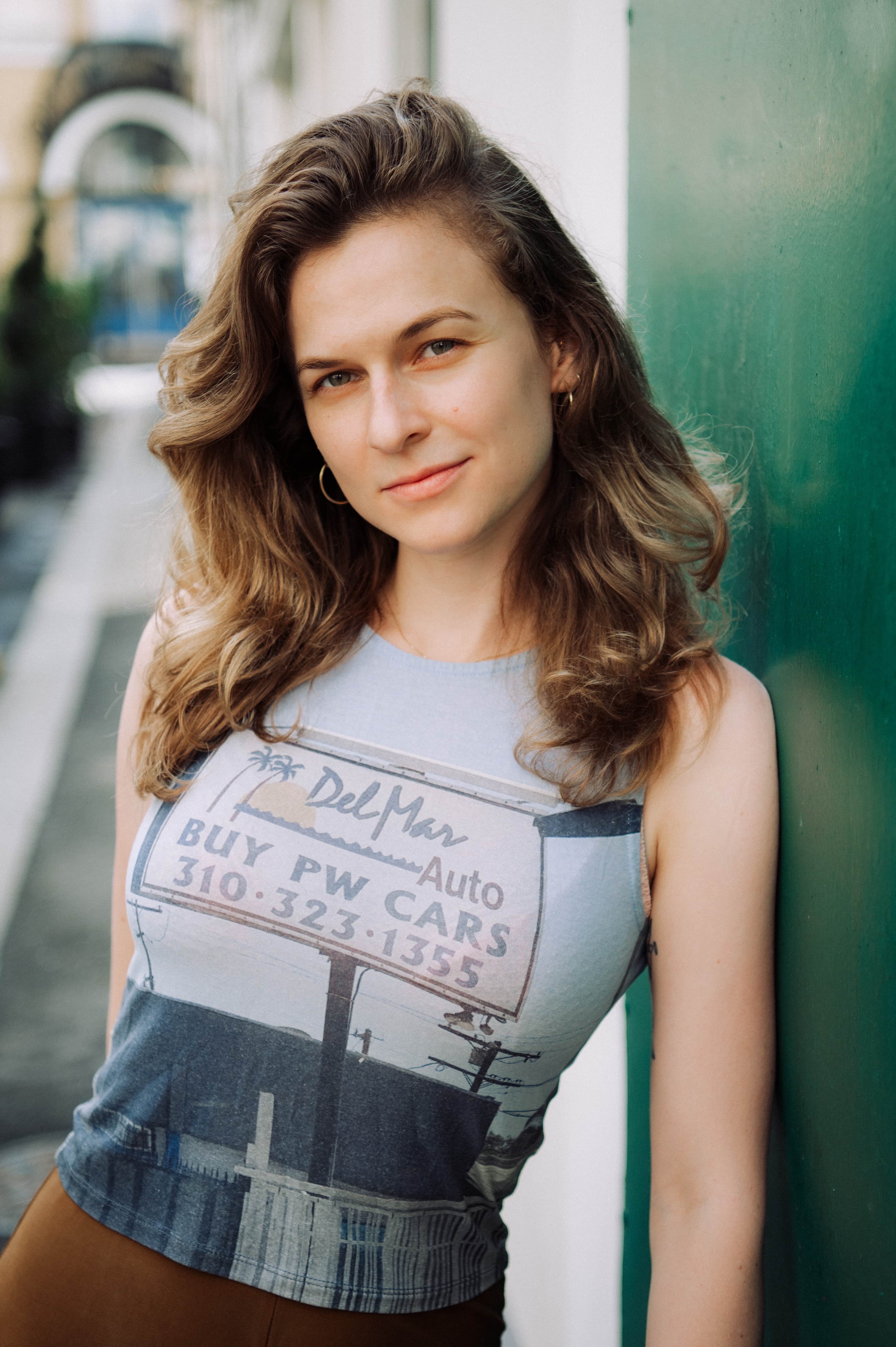 Woman with brown wavy hair over shoulders leaning against green wall