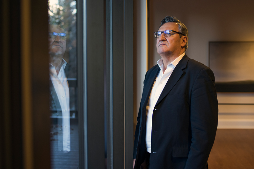 Brian Calliou looks out an office window with his reflection. 