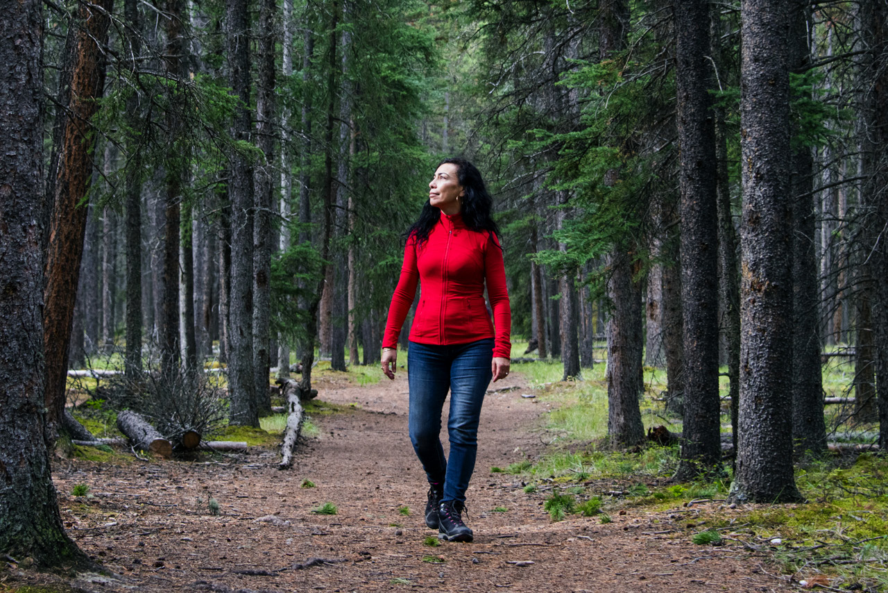 Carmen Aguirre walks through a forest surrounded by trees. 