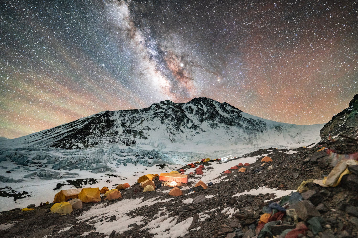 Tents scattered across a snowy mountain peak with a star filled sky. 