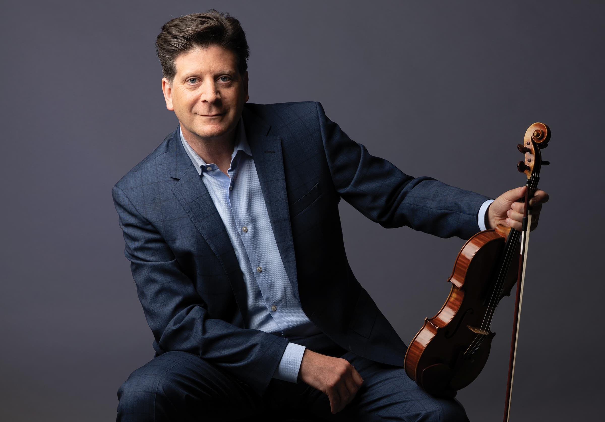 Barry Shiffman is seated on a chair with a violin resting on his knee.
