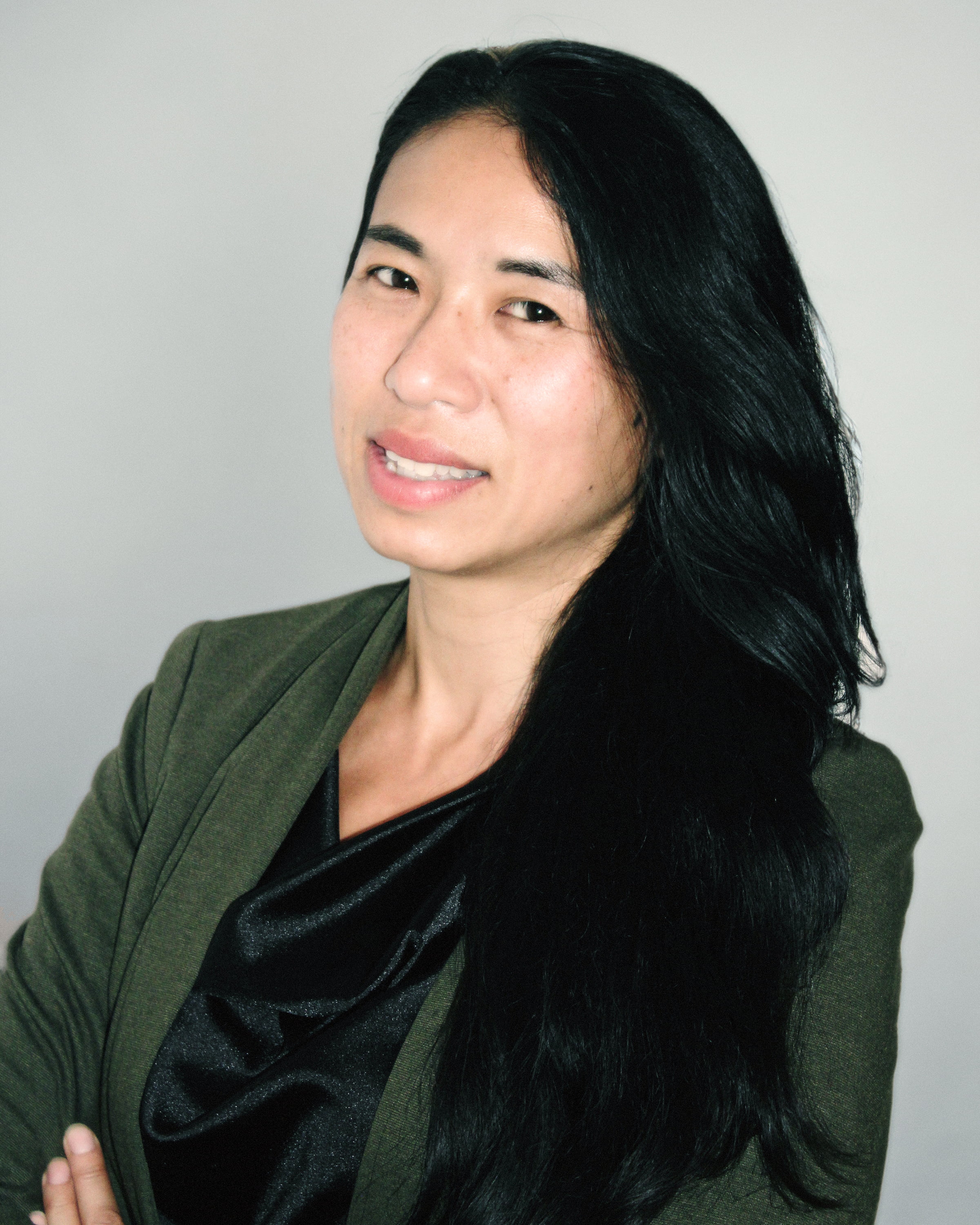 Woman with long black hair over shoulders and green sweater smiling at the camera