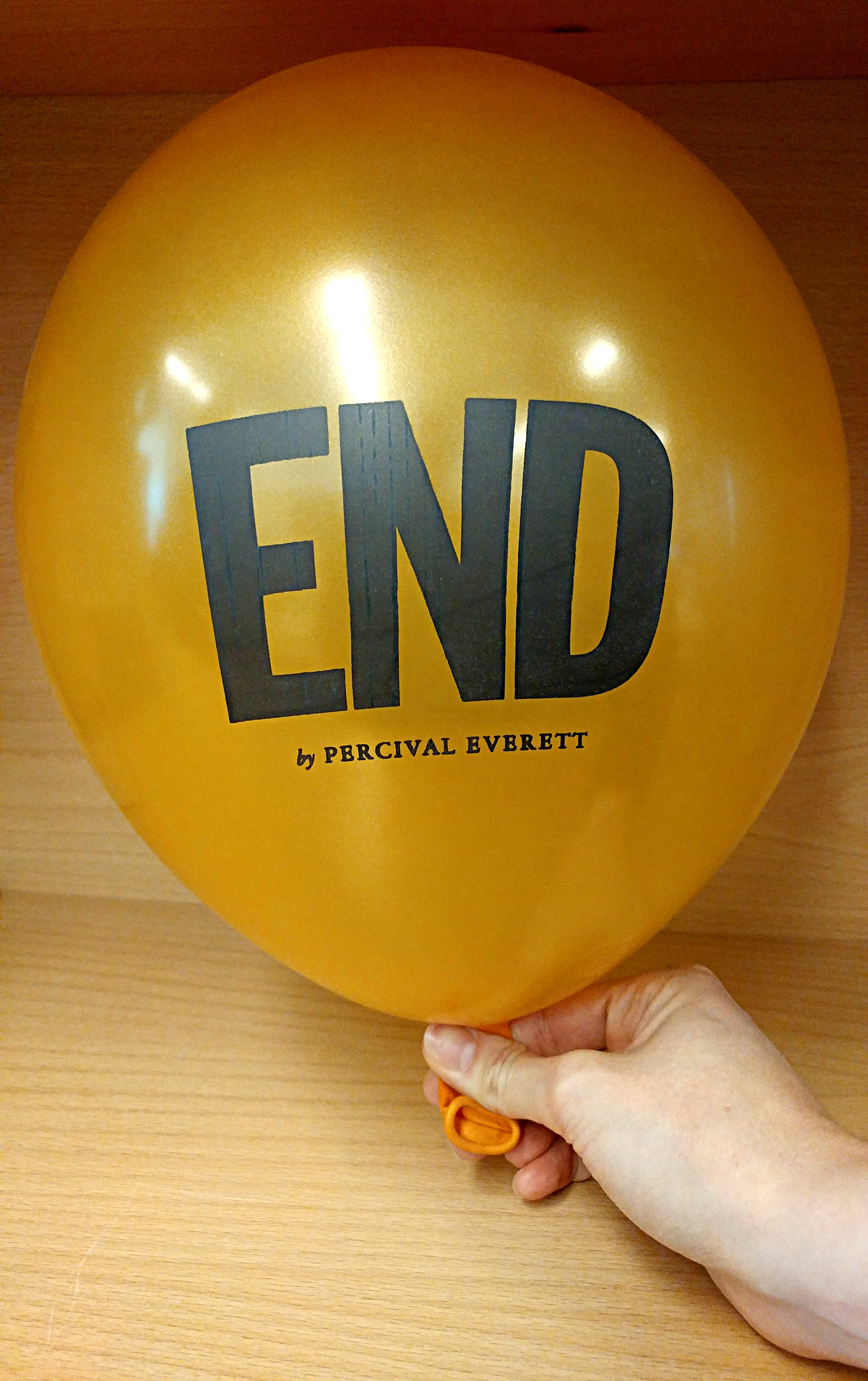 A golden balloon inflated with the text, "End by Percival Everett" printed on it. 
