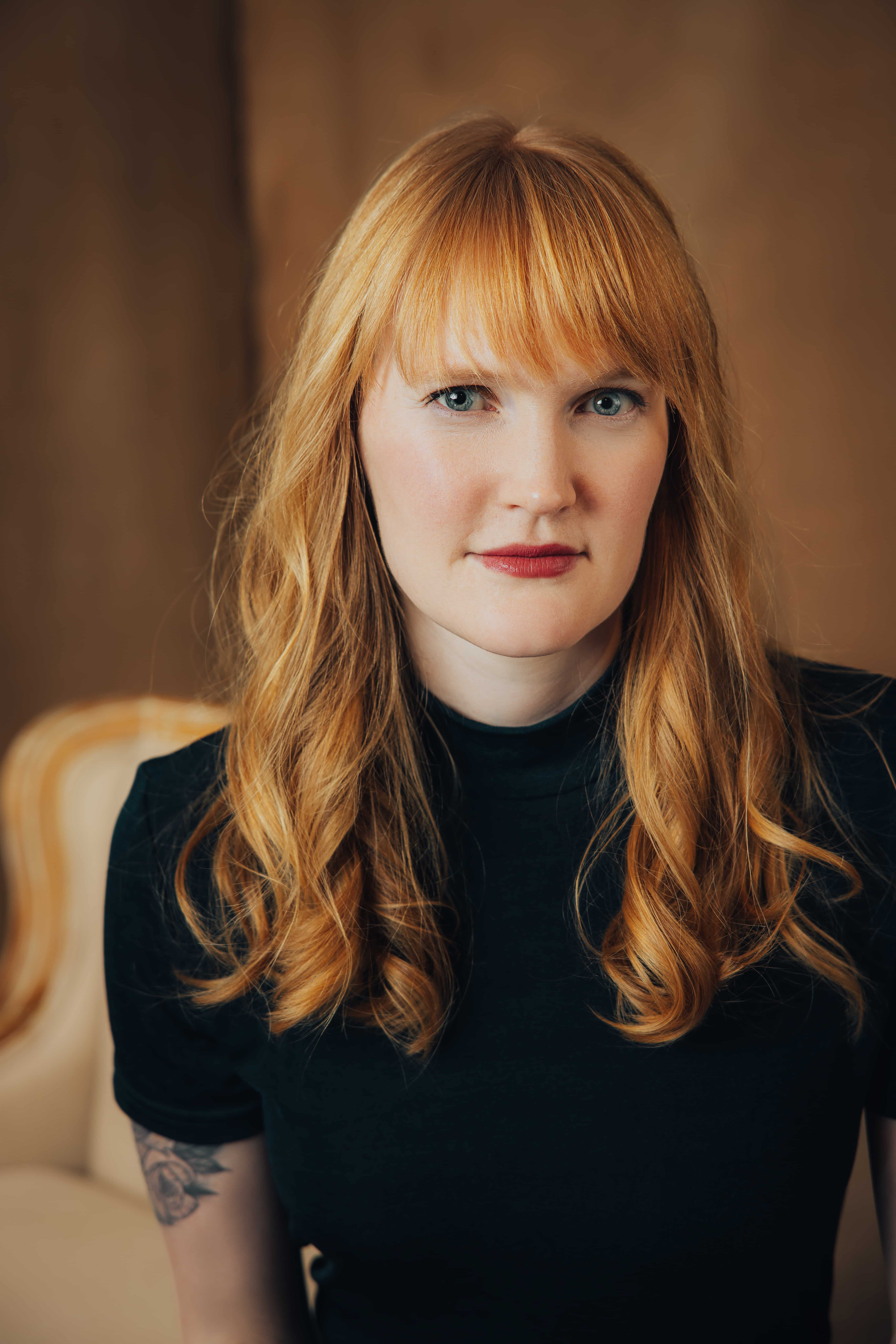 Woman with long red hair over shoulders and black t-shirt smiling slightly at camera