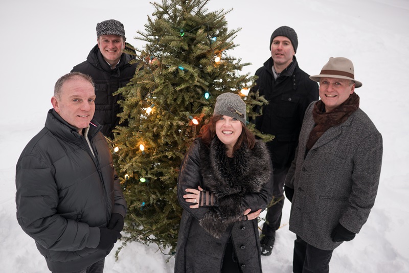 The Barra MacNeils stand around a Christmas tree in the snow.