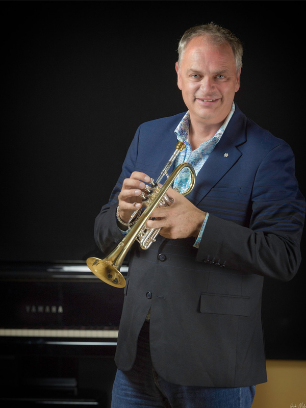Jens Lindemann holds a trumpet wearing a suit jacket and jeans.