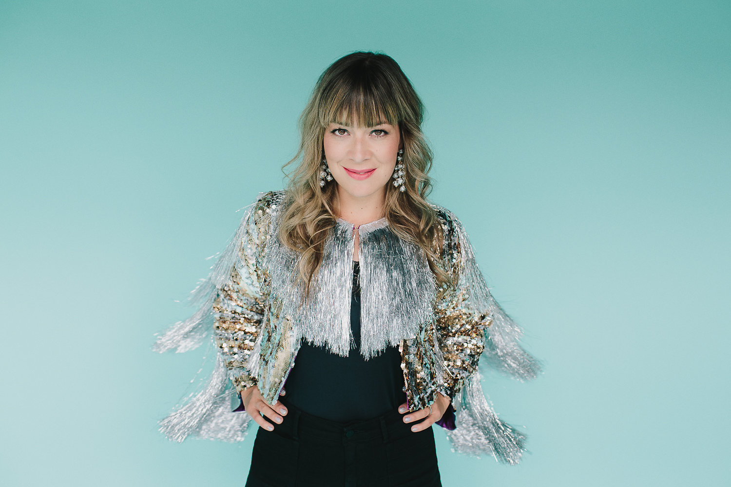 Jill Barber smiles standing with her hands on her hips in front of a blank background.