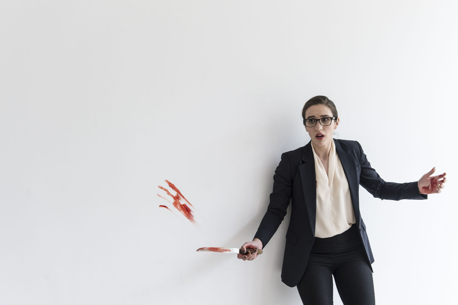 A shocked looking opera singer wears a suit and blouse while holding a bloodied knife.