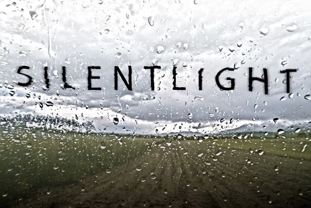 Opera. Silent Light. The words are graphically depicted in black over a rained upon window looking out at a field. 
