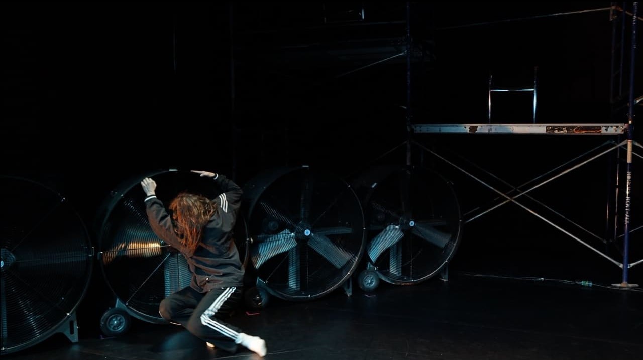 Photo of dancer on stage with industrial fans and scaffolding