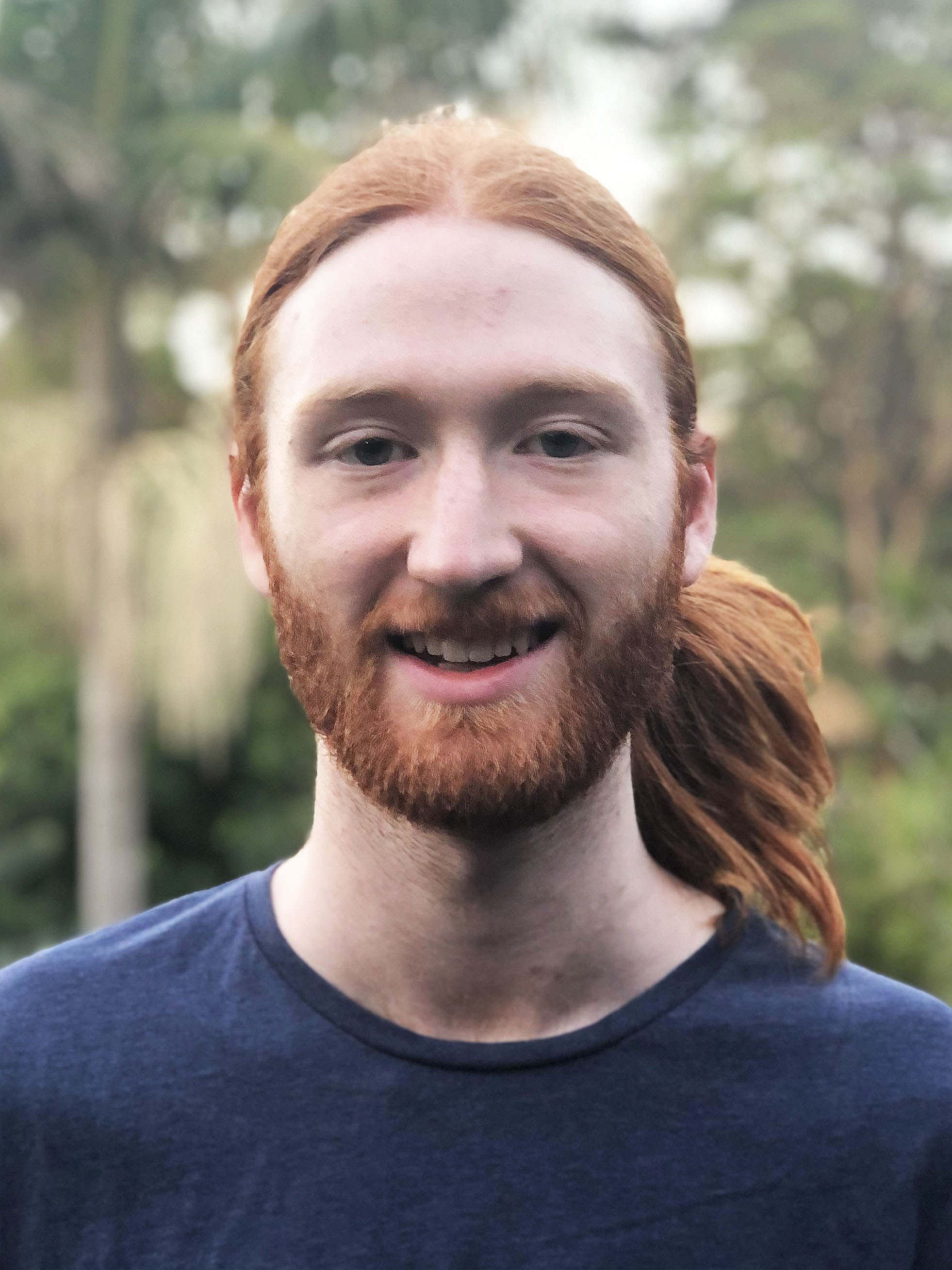 Man with long pulled back hair in a blue t-shirt smiling at the camera