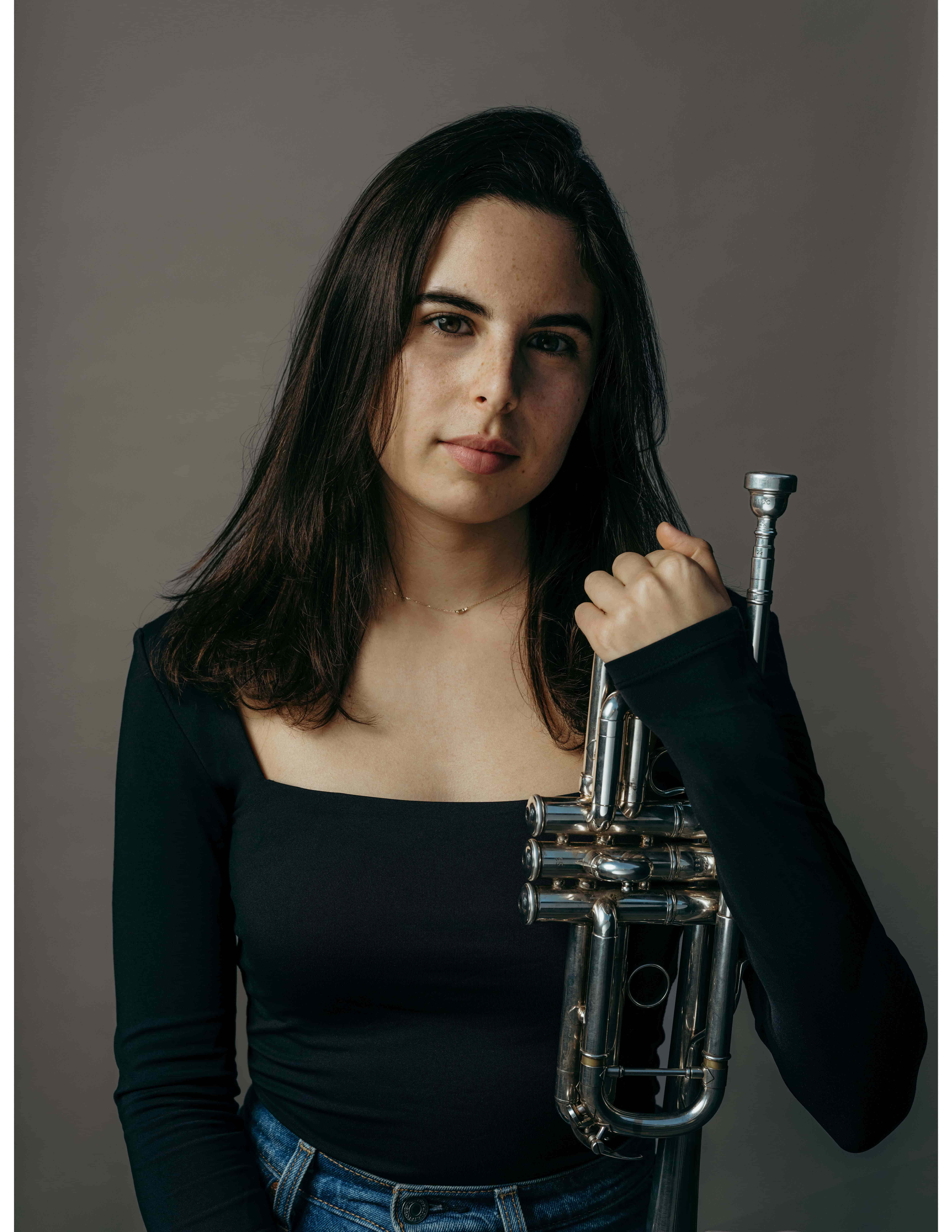 Woman posing by holding trumpet upright resting against her body