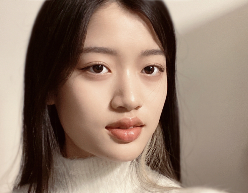 Close up headshot of a woman with brown hair and wearing a white sweater looking directly at the camera