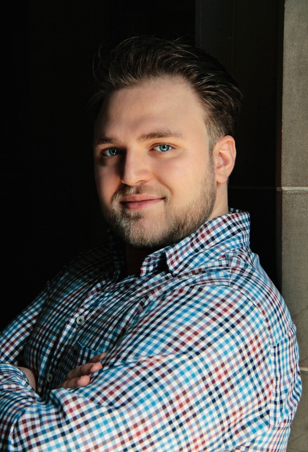 Man in plaid shirt arms crossed leaning against wall