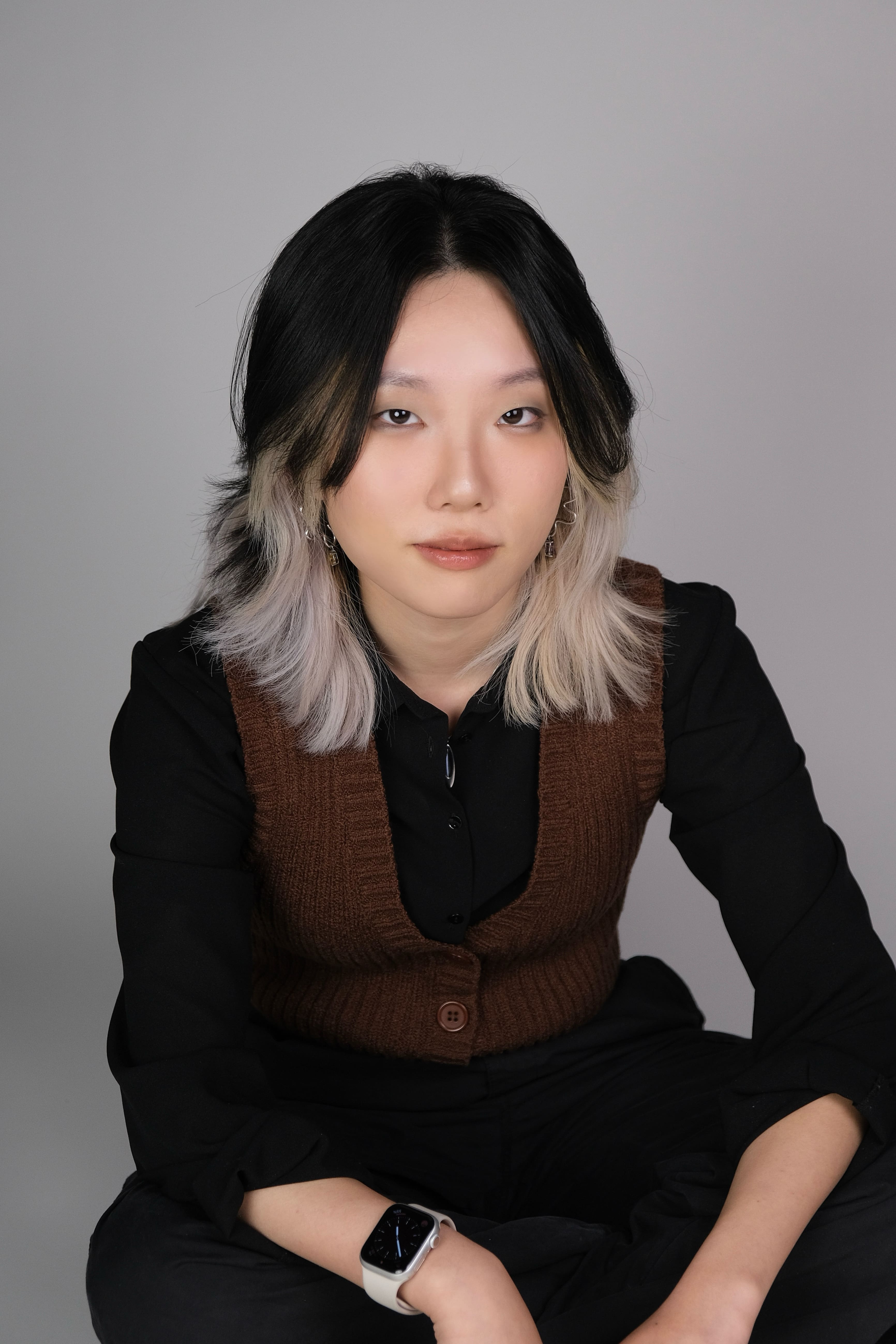 Woman wearing a vest staring directly at the camera and sitting with elbows on knees
