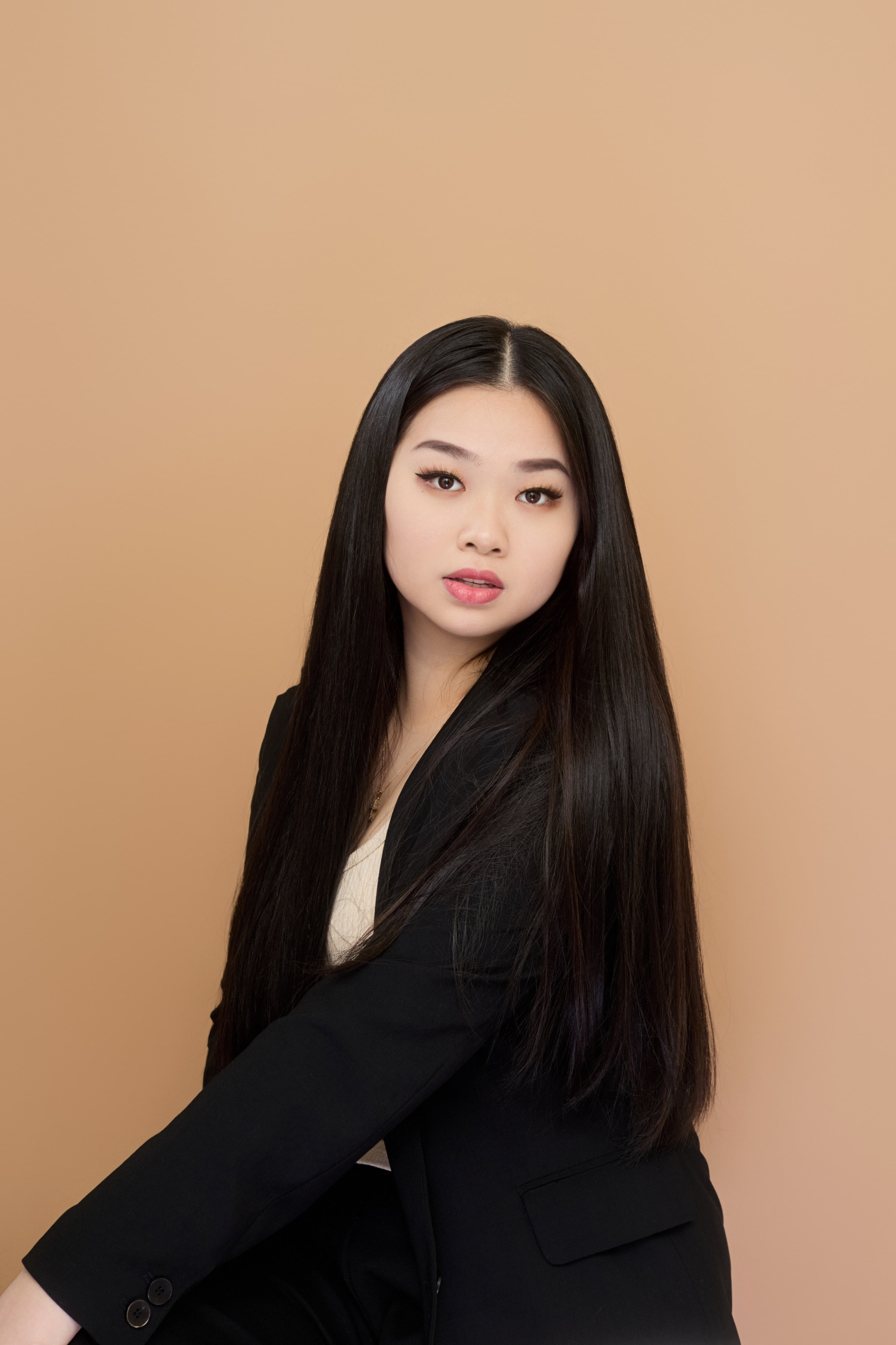 Woman sitting in suit jacket in front of orangish background looking directly at the camera