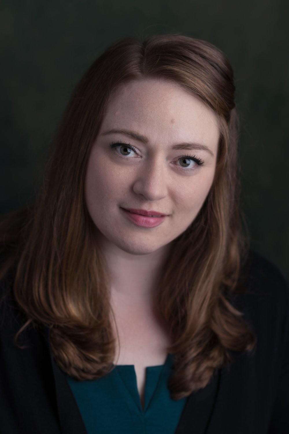 Woman with red hair flowing over shoulders smiling lightly and directly at camera