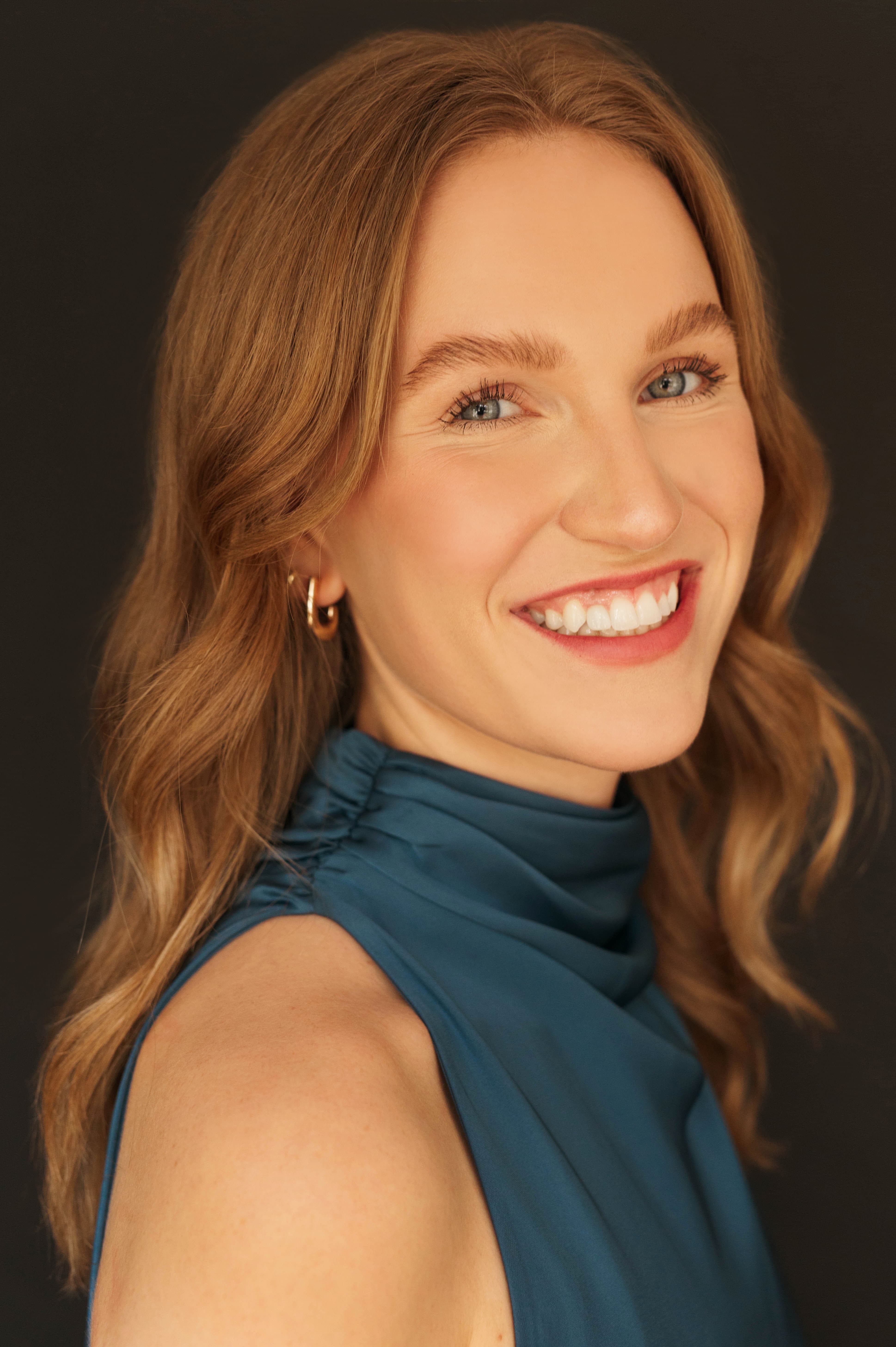 Woman smiling broadly at camera with flowing red hair and a teal halter dress