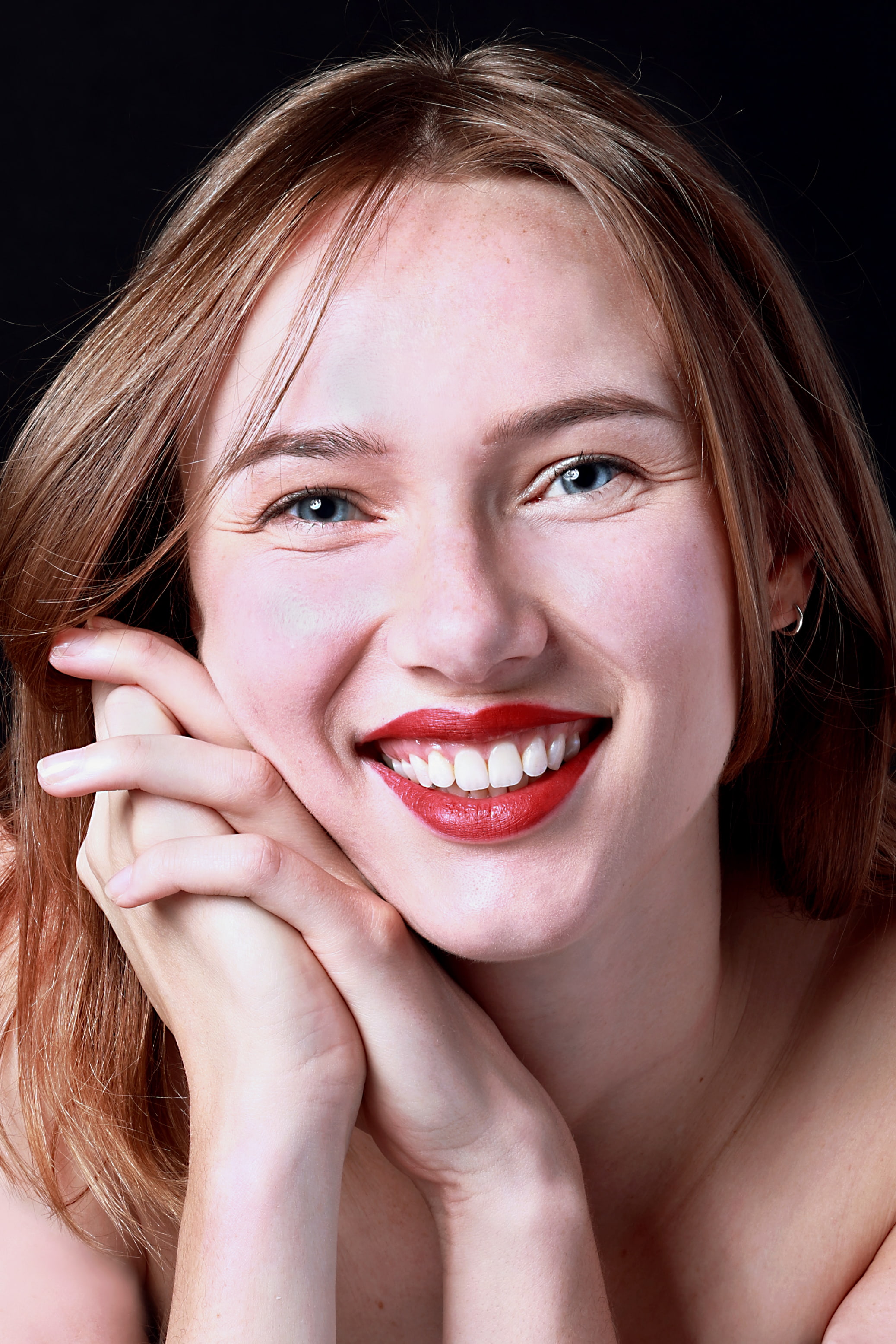 Close up shot of woman smiling broadly at camera with face leaning against clasped hands