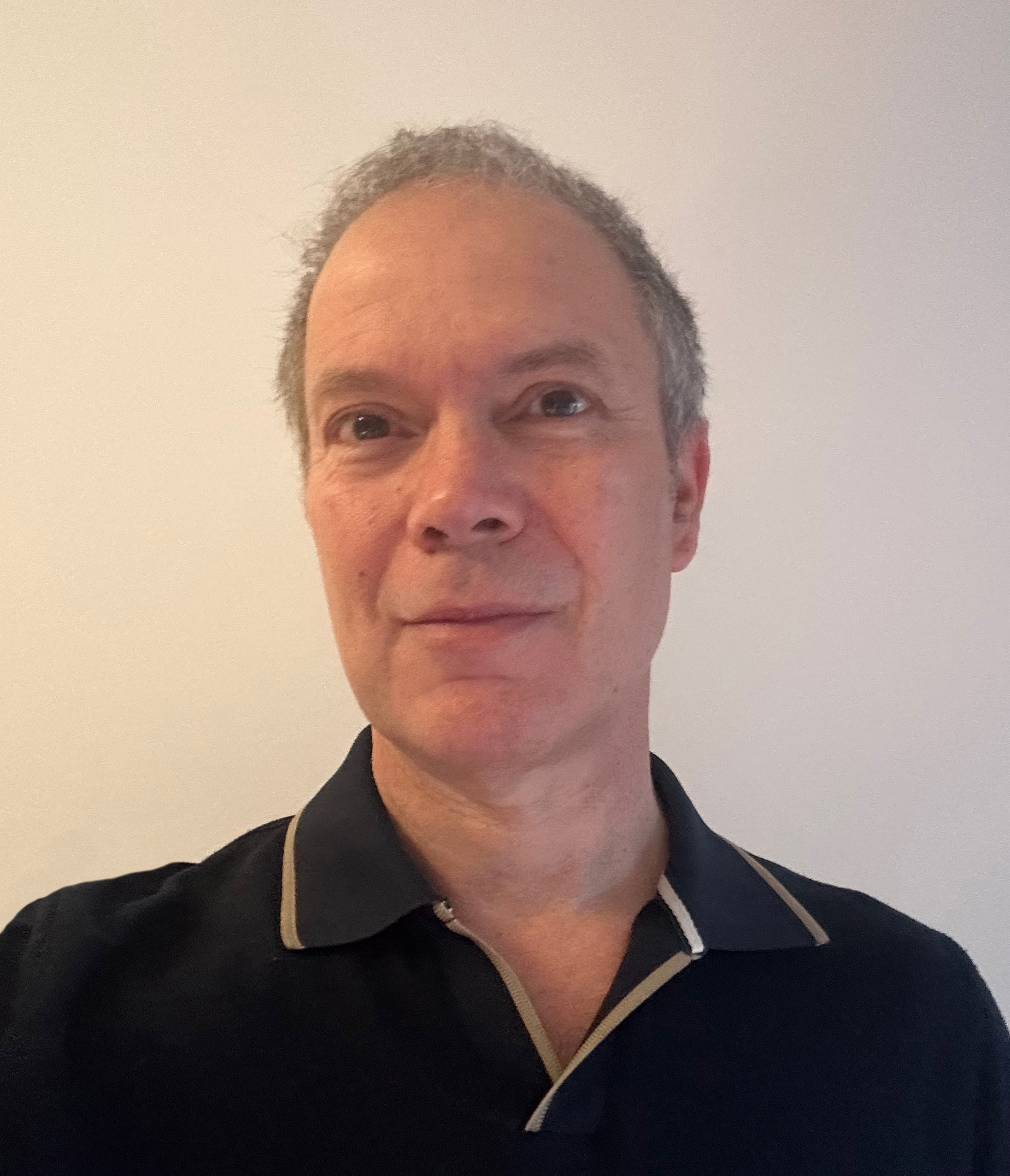 Man smiling directly at camera wearing close cropped hair and a black polo shirt