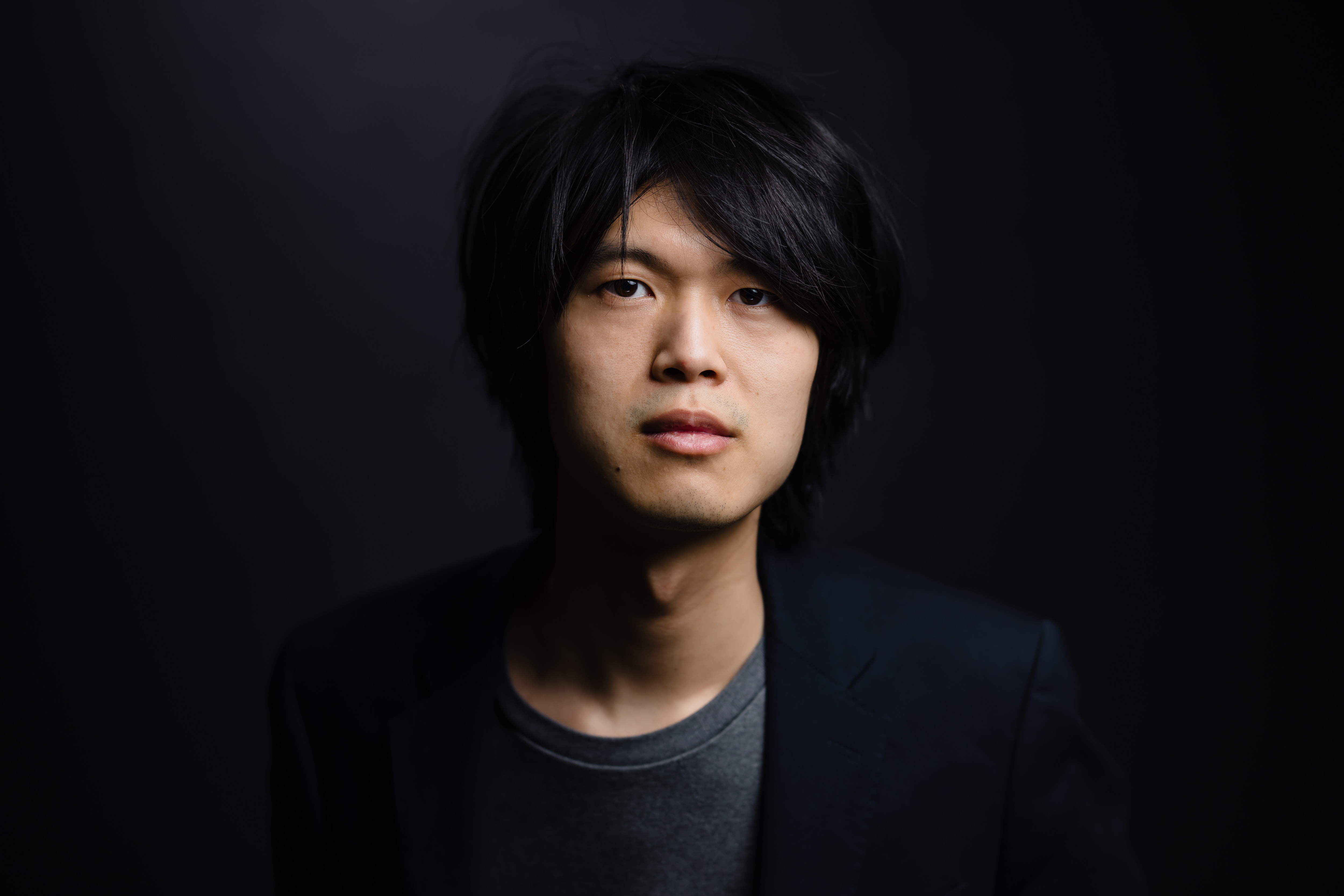 Man staring directly at camera in dark suit and dark room