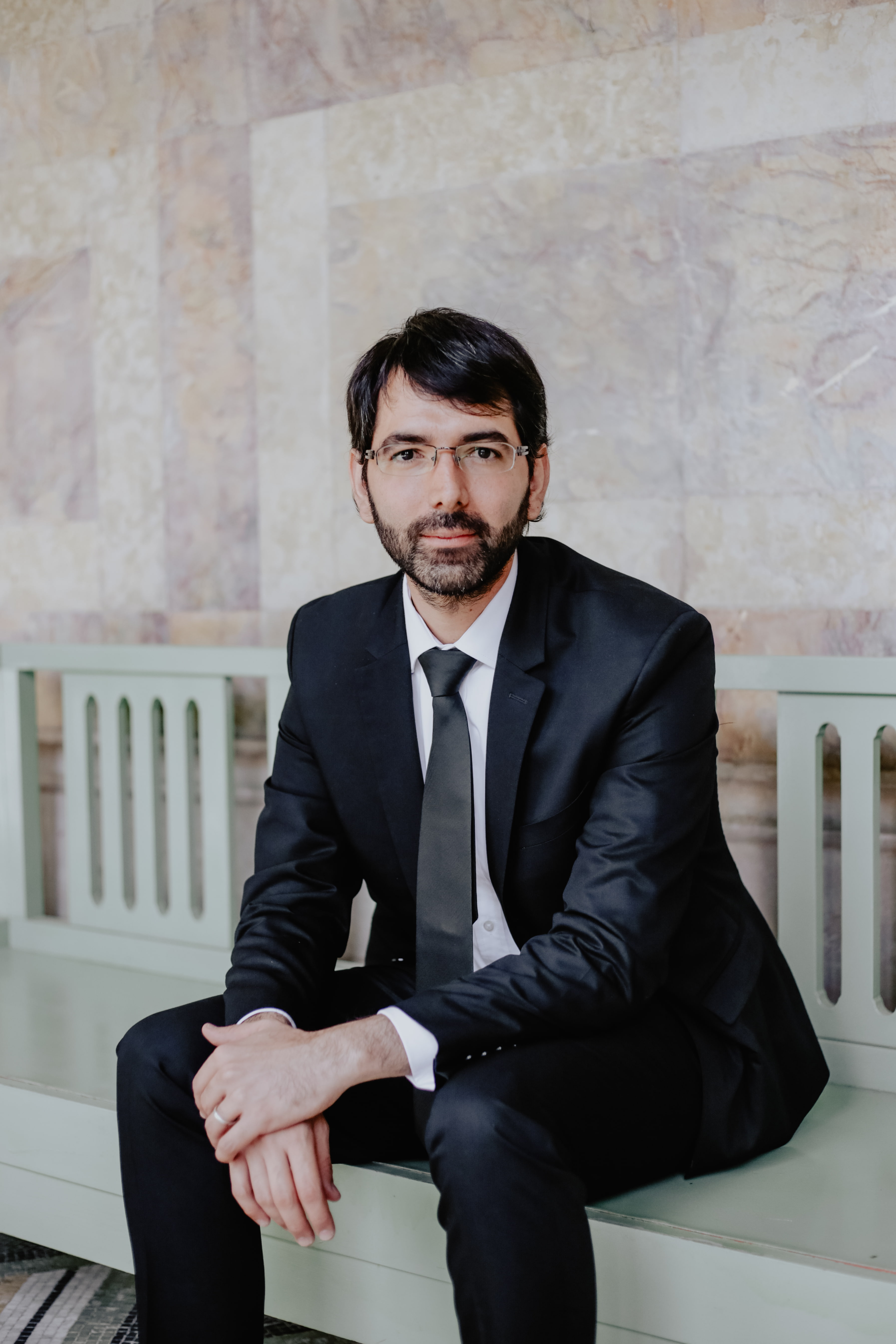 Man sitting on a bench in a suit with hands clasped in front of him