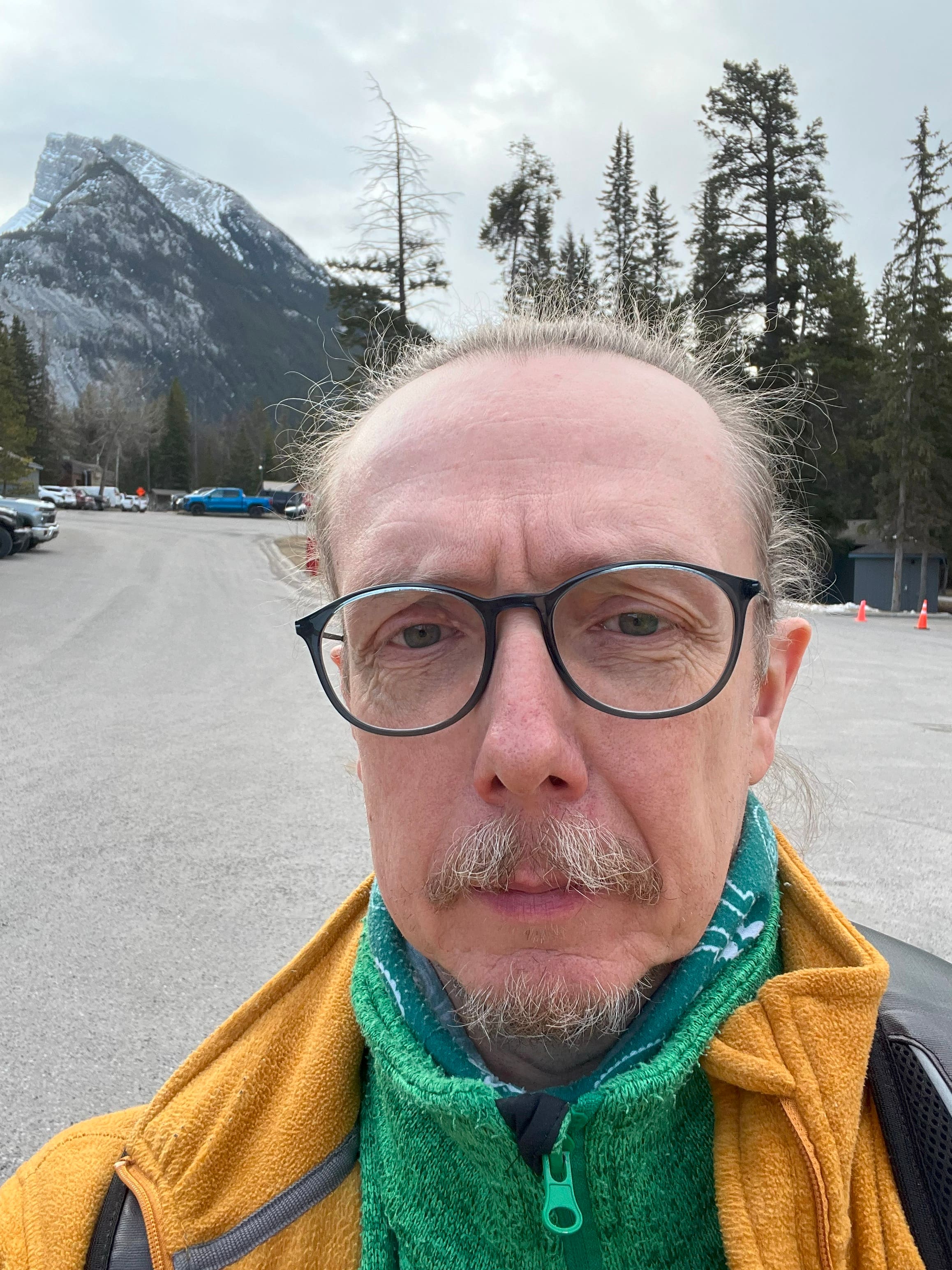 Man with glasses and pulled back hair standing in front of Rundle Mountain