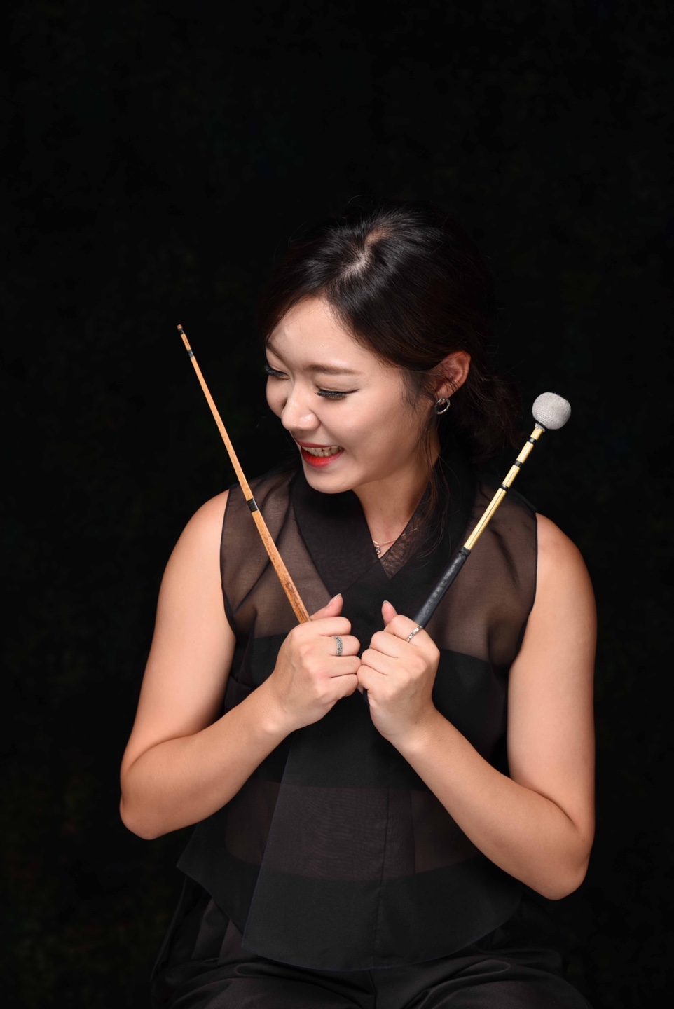 Person smiling with drum sticks looking off to the side