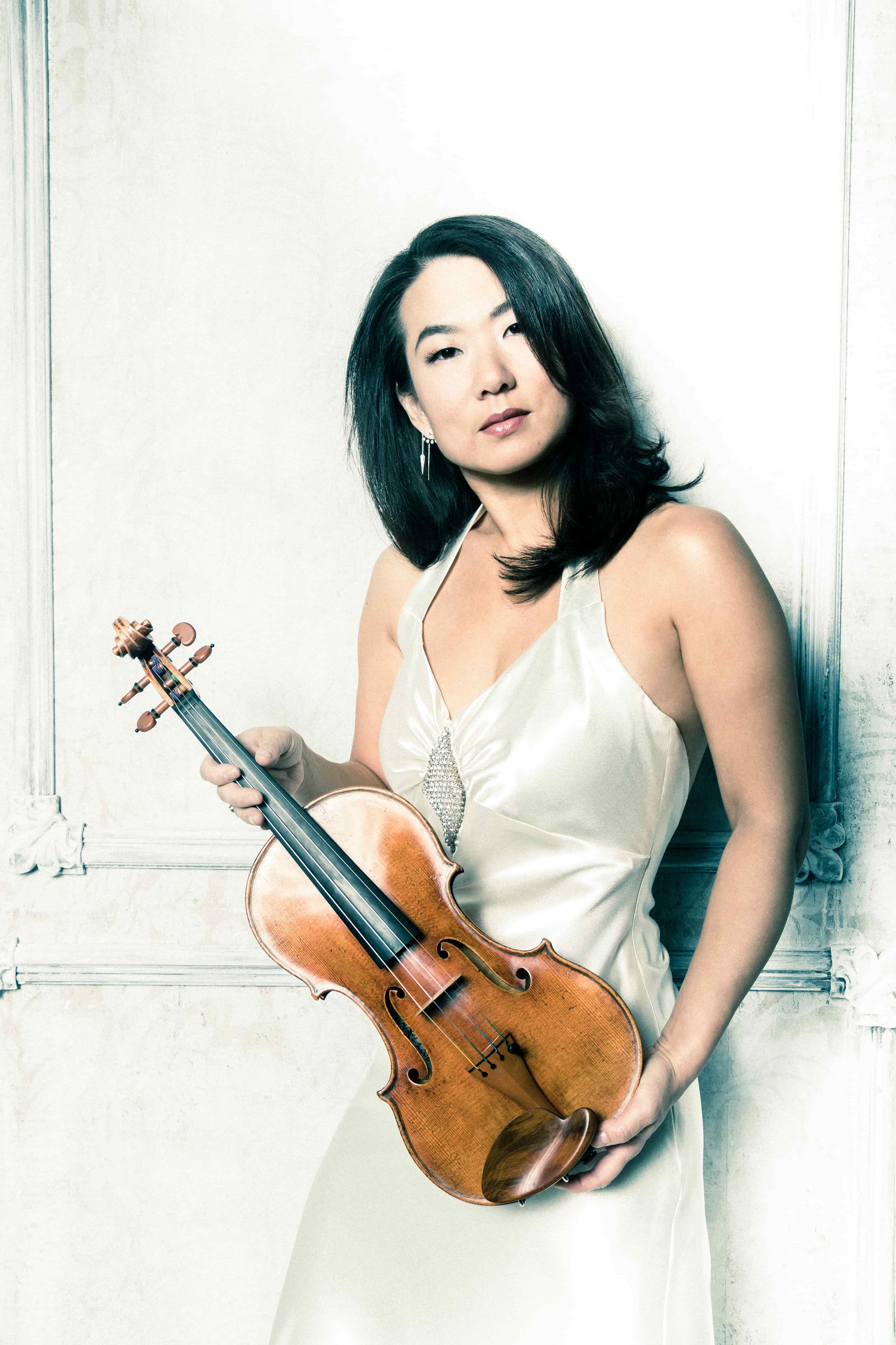 A woman in a white dress is holding a violin