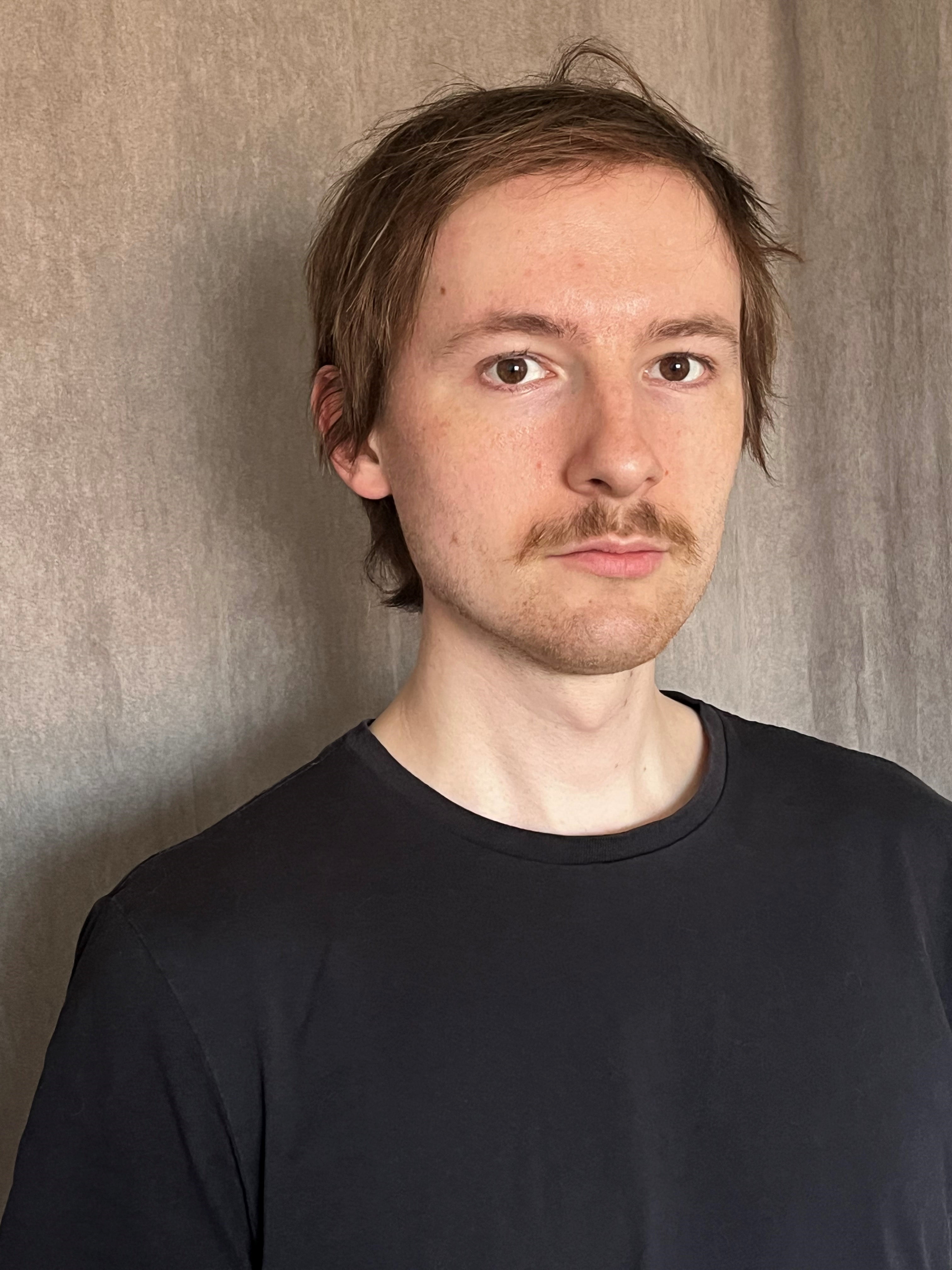 Man in black t-shirt standing against wall and looking at camera