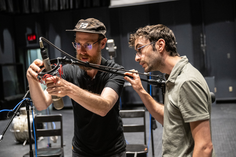 Two audio engineers are adjusting a microphone stand in a studio