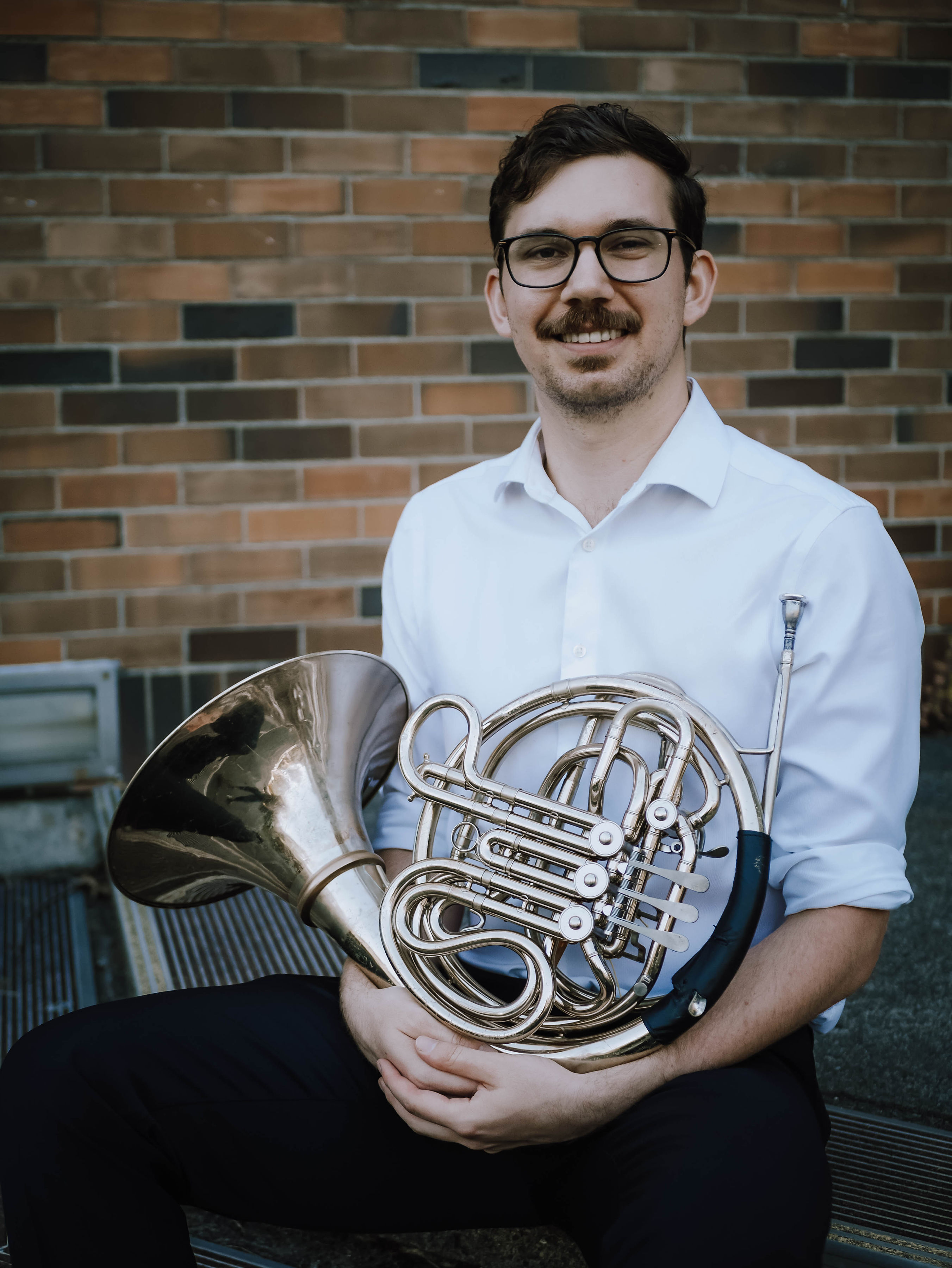 Man smiling at camera holding french horn on lap