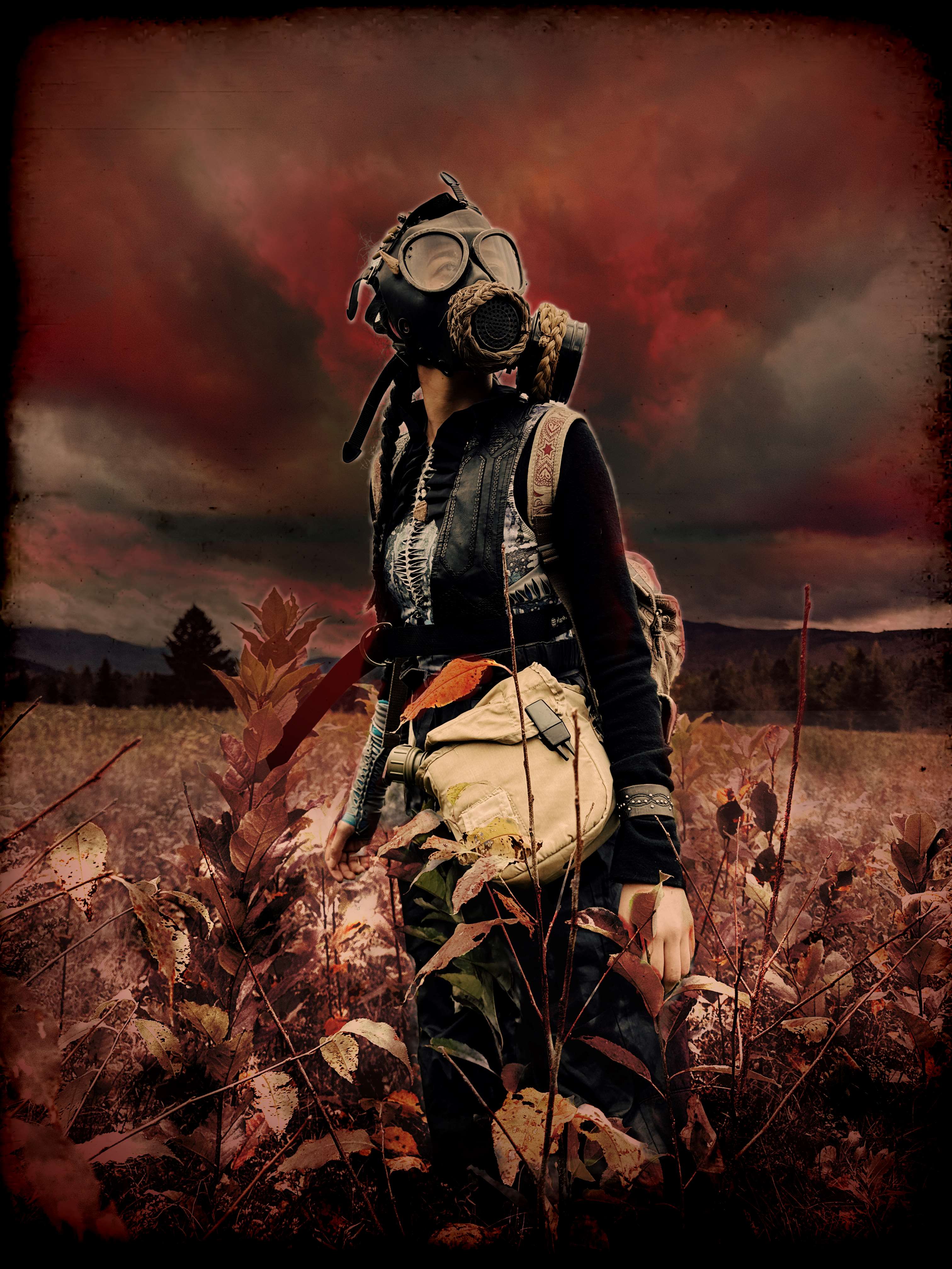 Woman standing in a field with dark, red sky and red tinted landscape. Woman wears gas mask, goggles and carries a large
