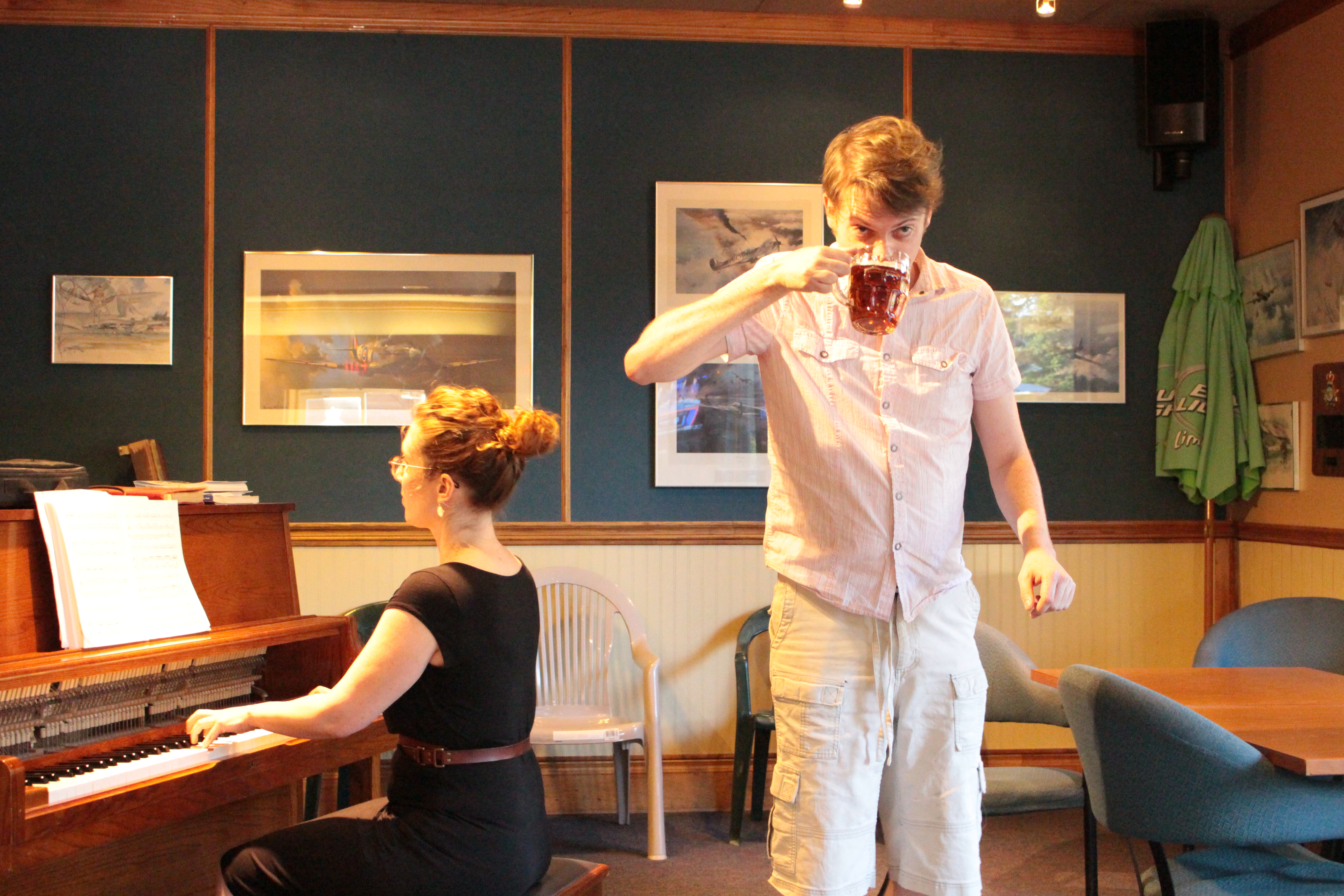 Woman plays piano while standing man takes a drink