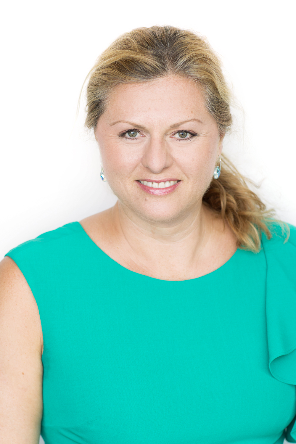 A white woman with blonde hair in a ponytail wearing a bright teal blouse.