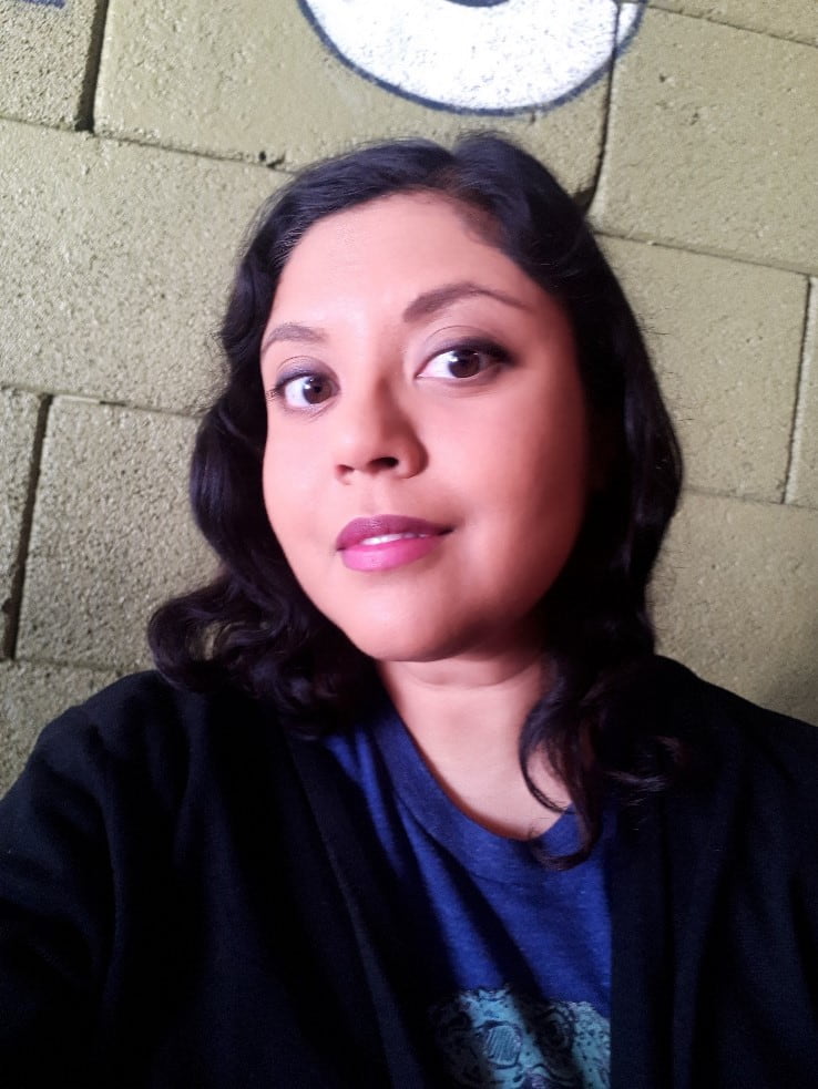 Woman with dark hair and wearing a blue t-shirt and cardigan.