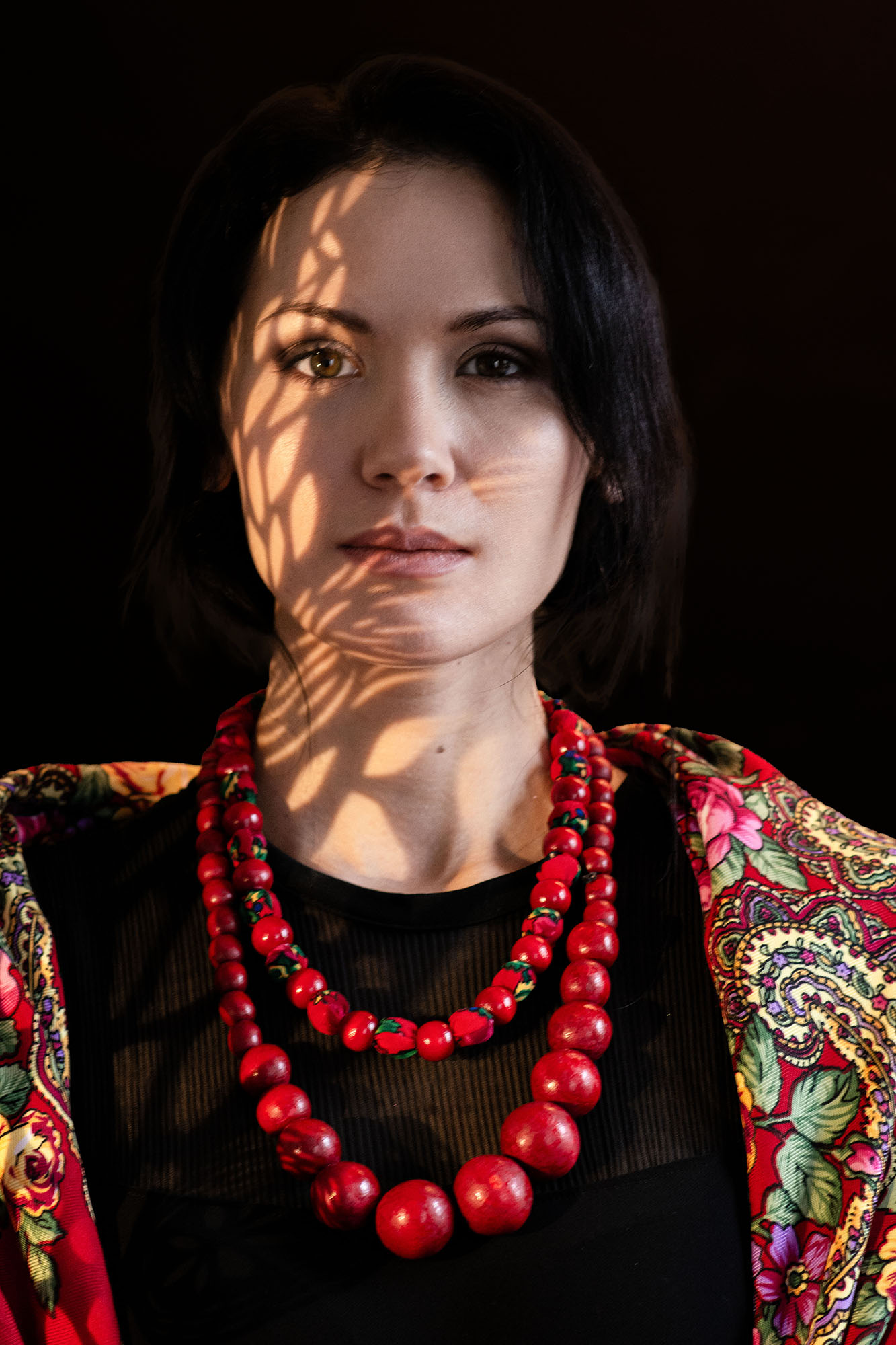 Person looking into the camera wearing a red necklace and colour top