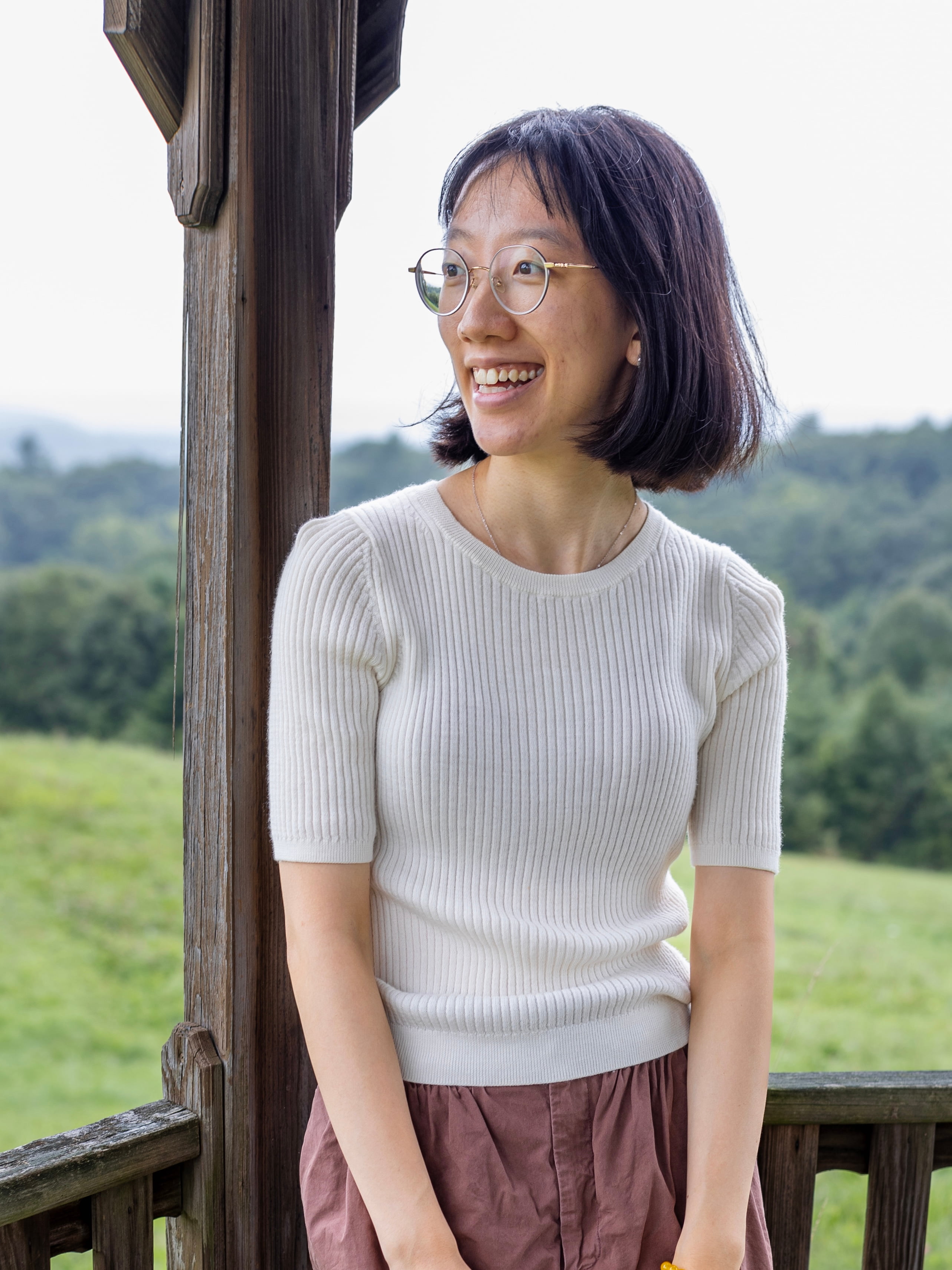 Person with shoulder length hair and white shirt looking into the distance smiling