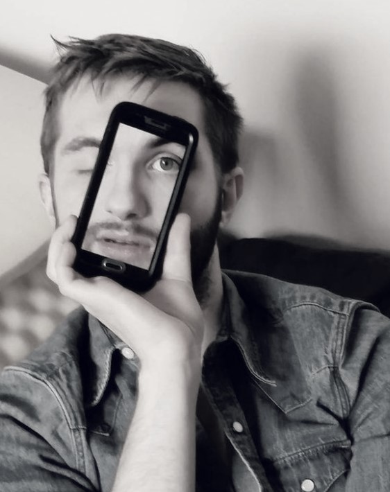 Man holding phone in front of face with the image of his face on the phone screen so that the full face is visible