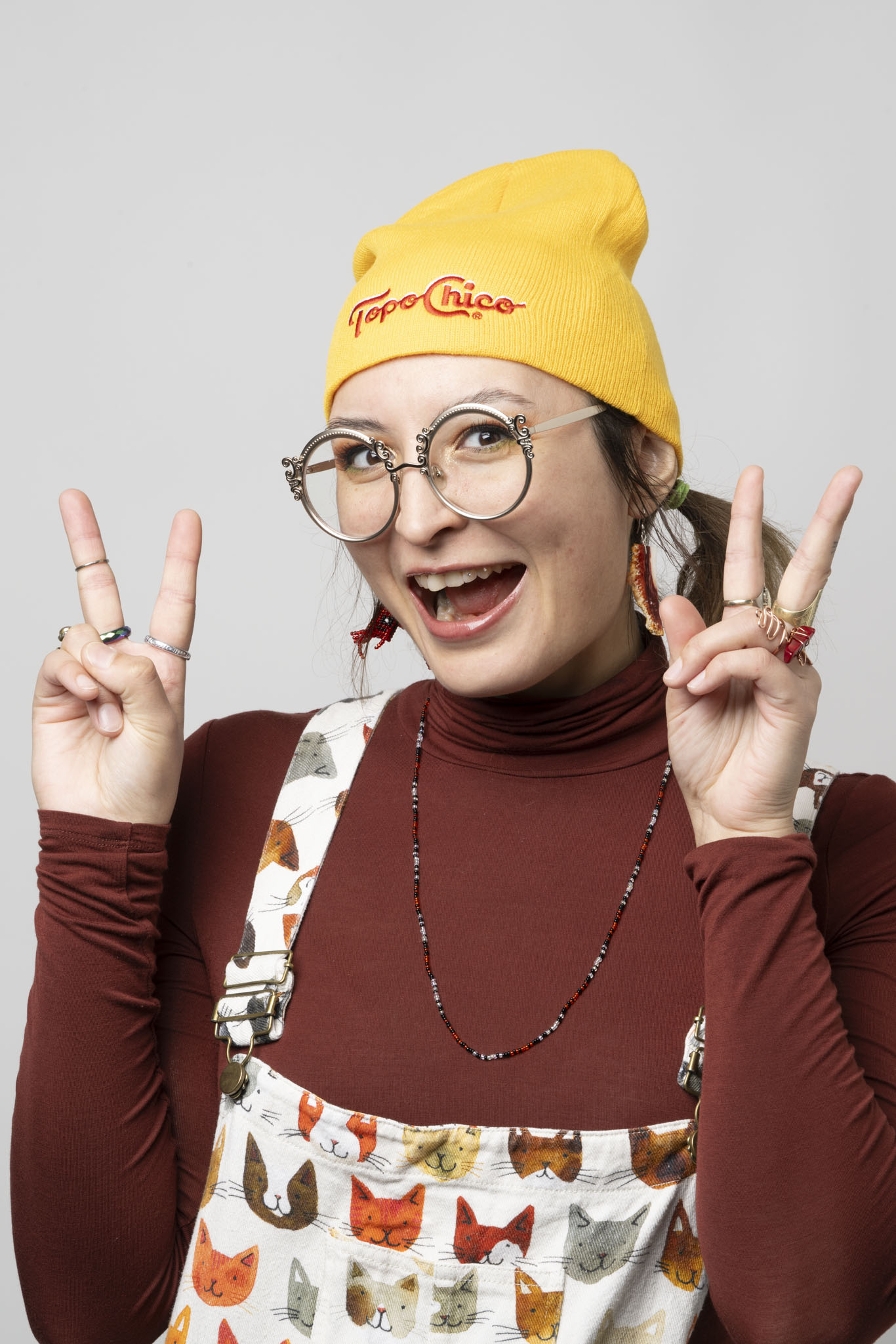 Woman with large smile and yellow toque giving two peace signs to the camera