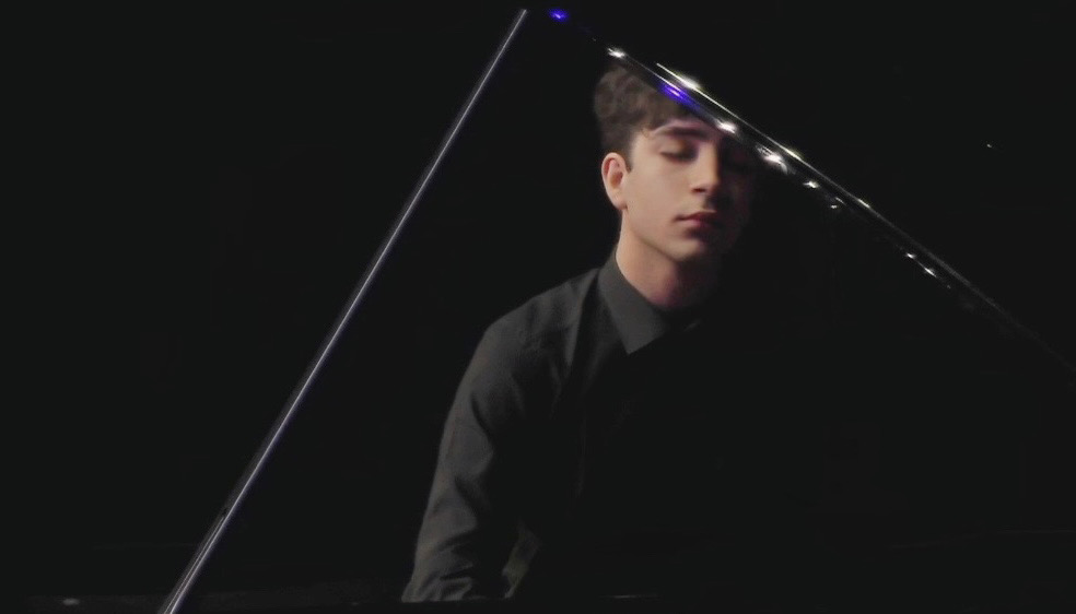 Dark shot of a man standing behind a grand piano as if playing while standing
