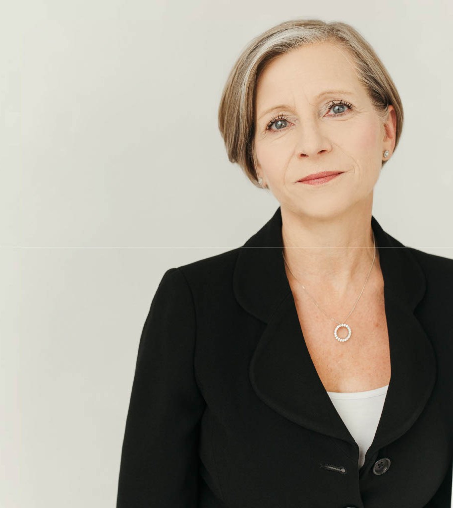 Woman with short blonde hair and black jacket smiling softly at the camera