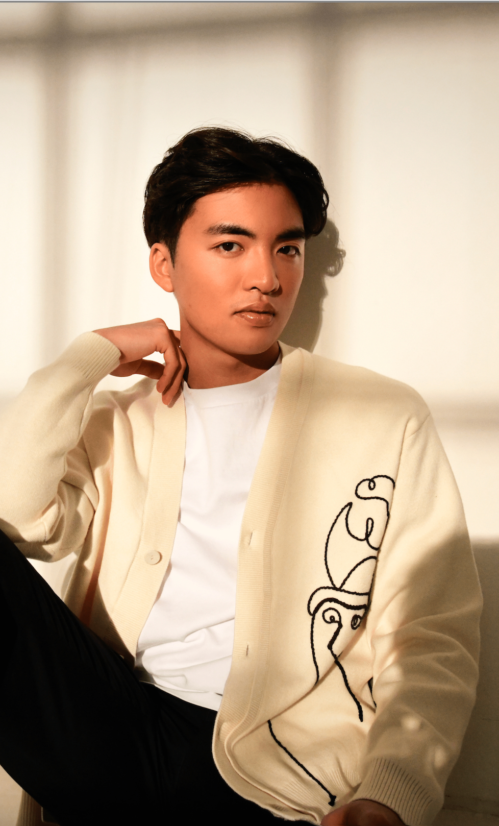 Man in the shadow of a window looking at the camera in a casual white artsy sweater