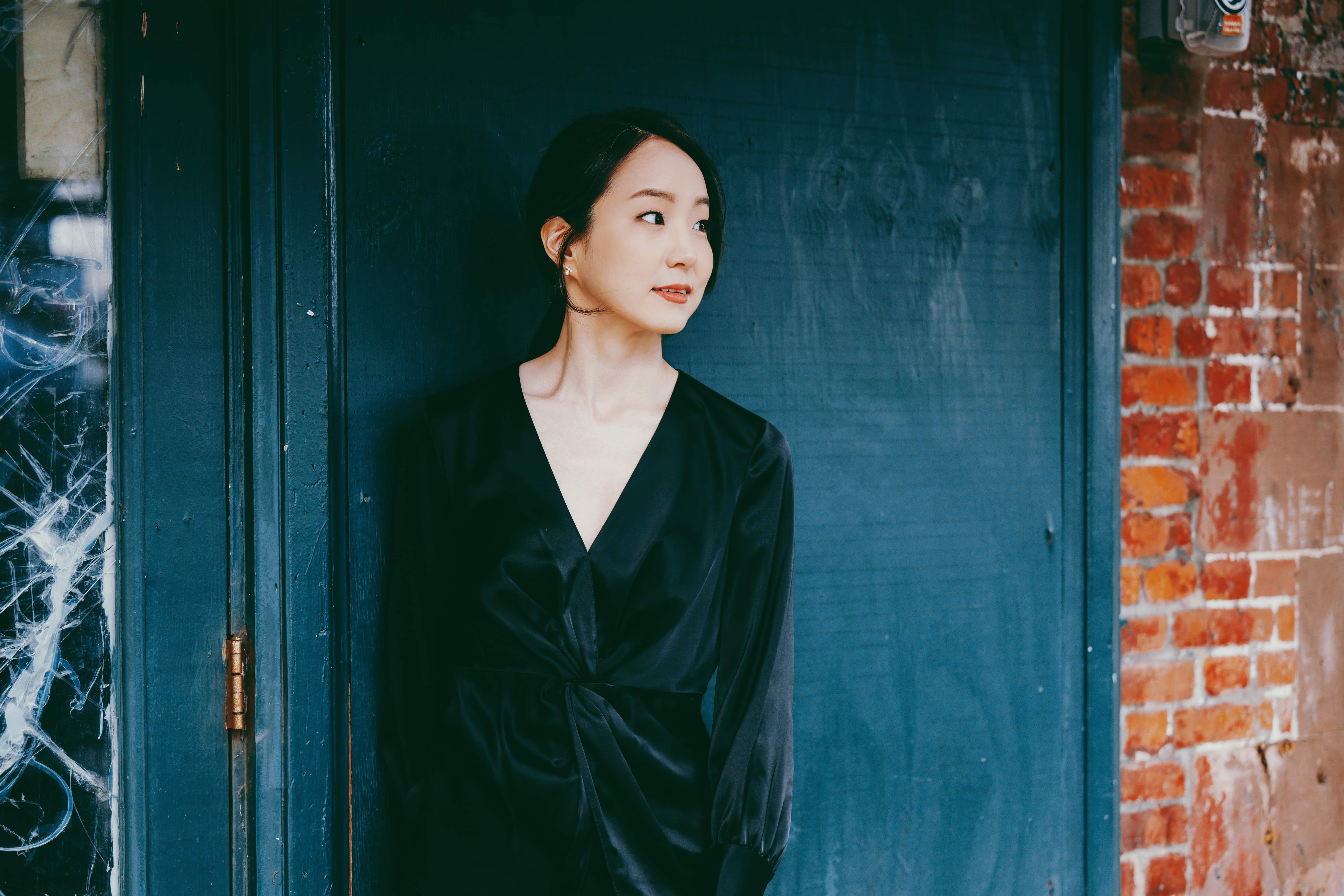 Woman in black dress standing in front of blue door looking towards the right of the camera