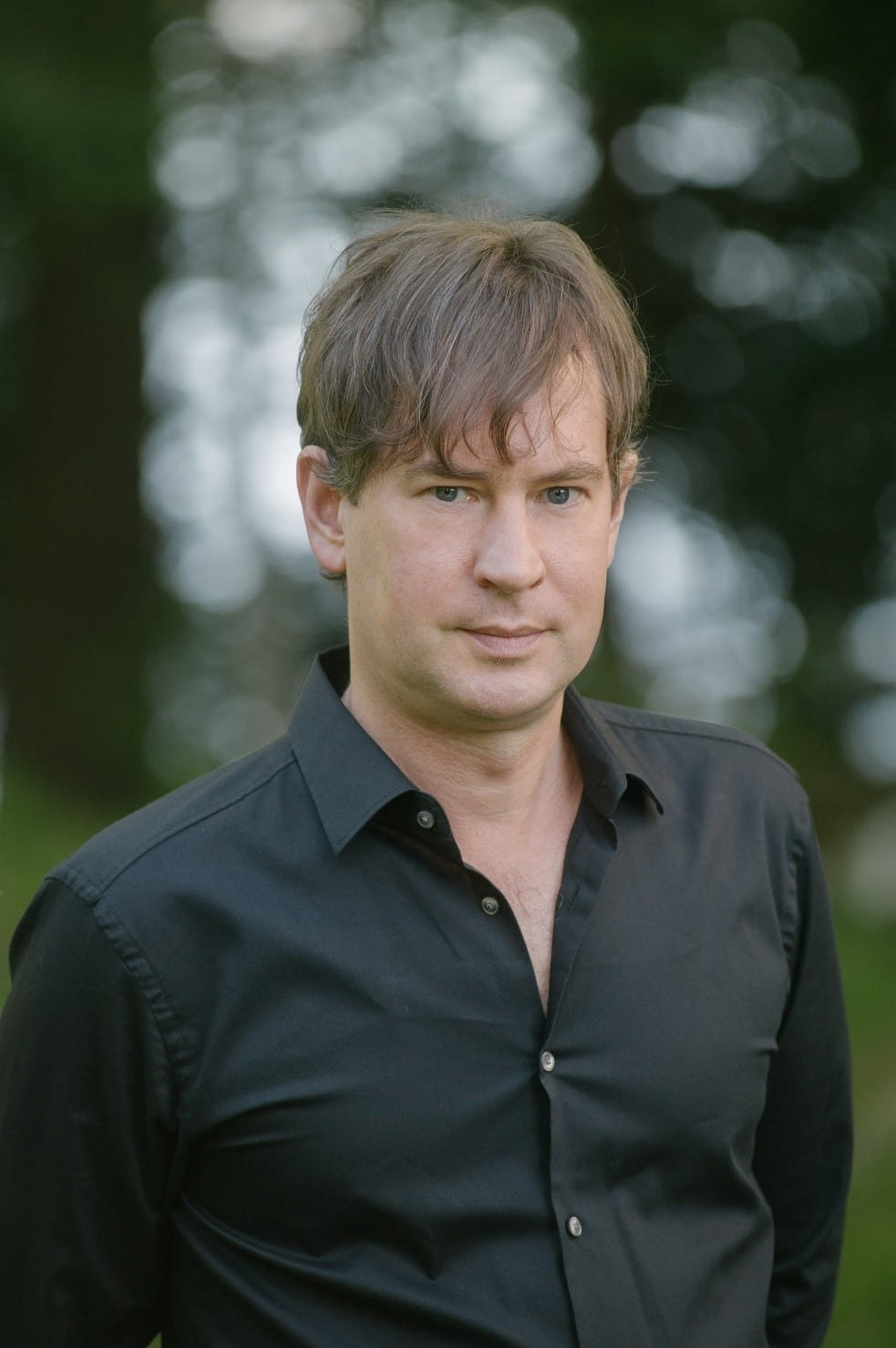 Taras Grescoe wearing a black shirt against a blurred background of trees